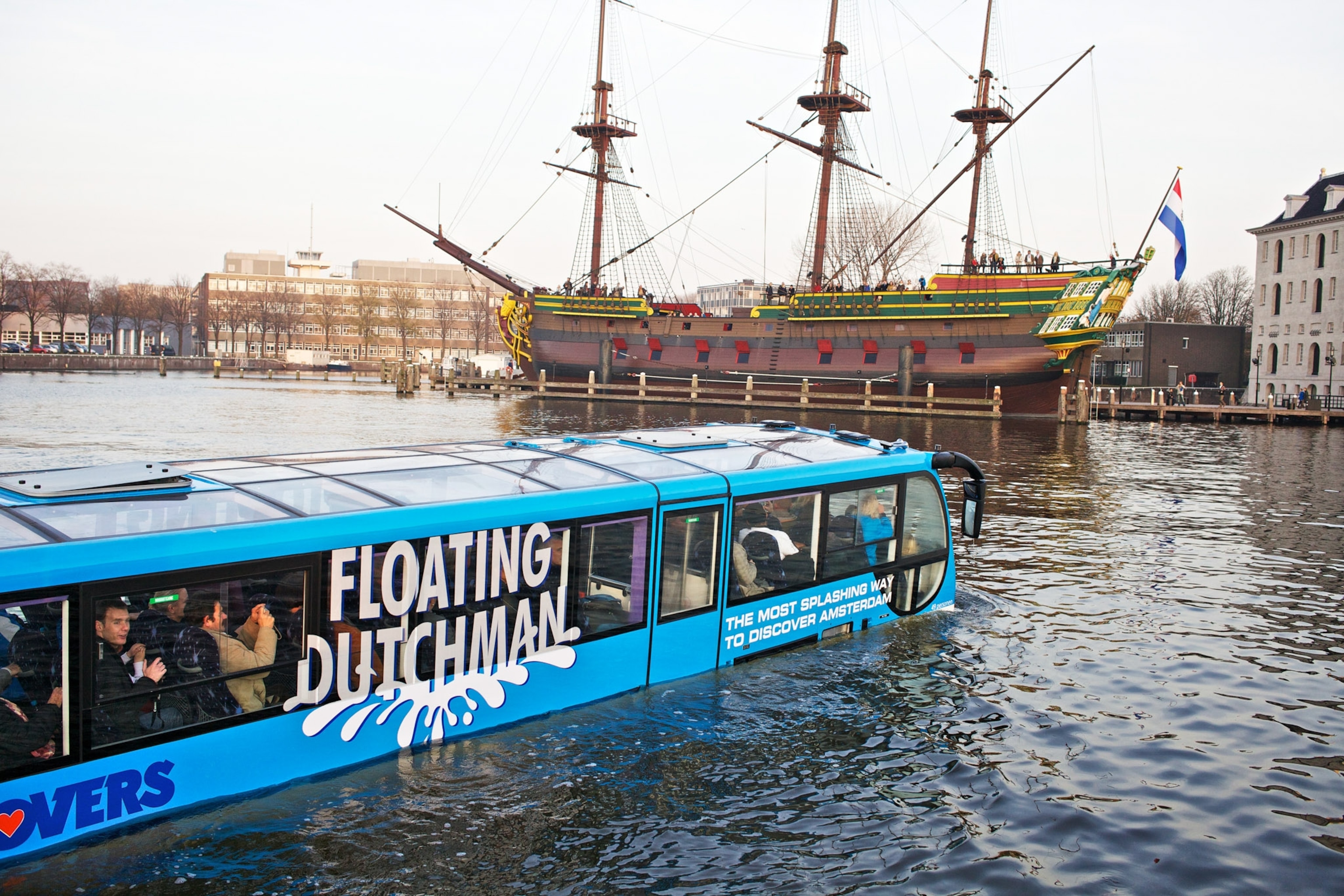People look outside and take pictures from their water bus a boat sits in the distance.