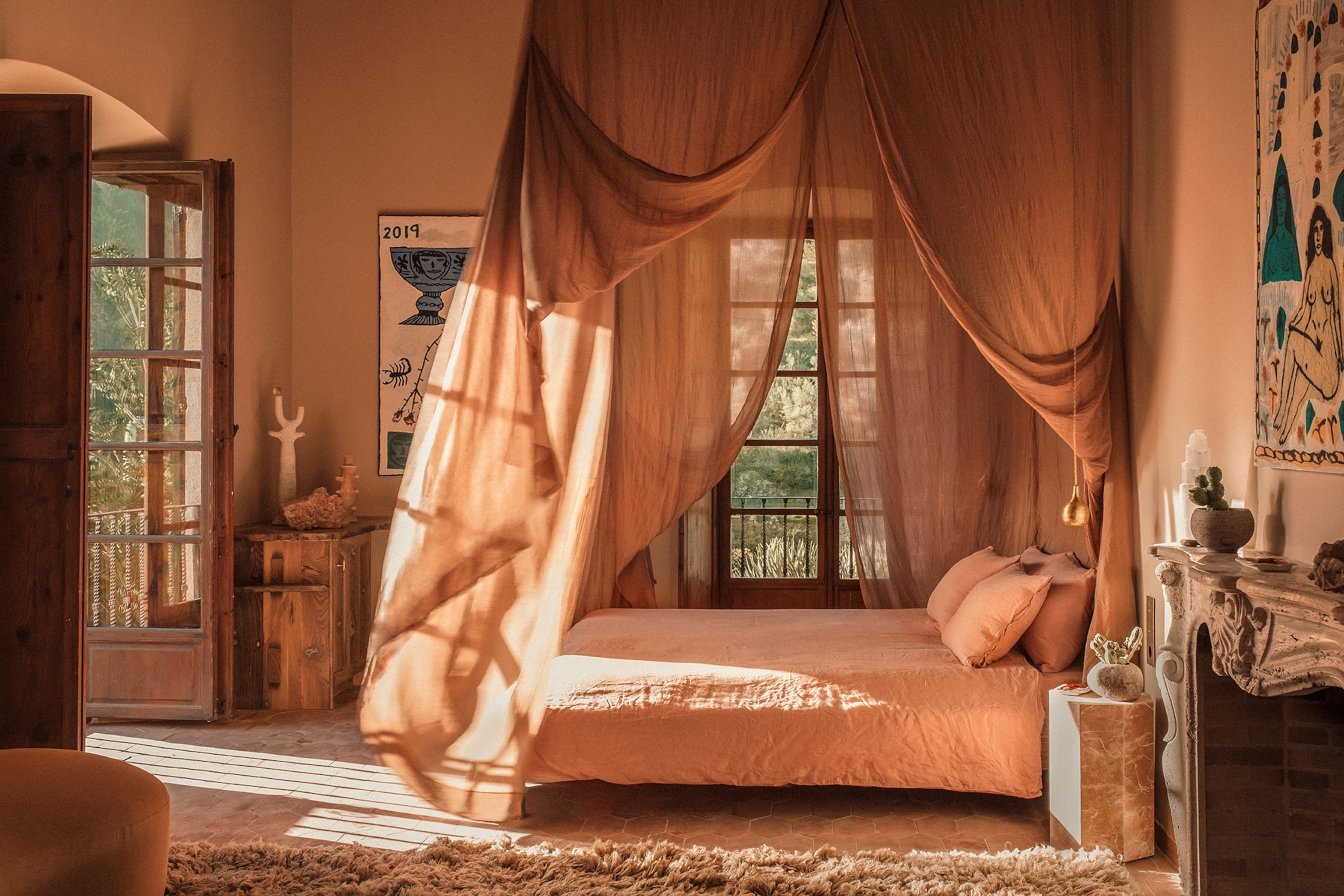 Pink toned bedroom with a canopy hanging above a double bed with wooden and marble furniture