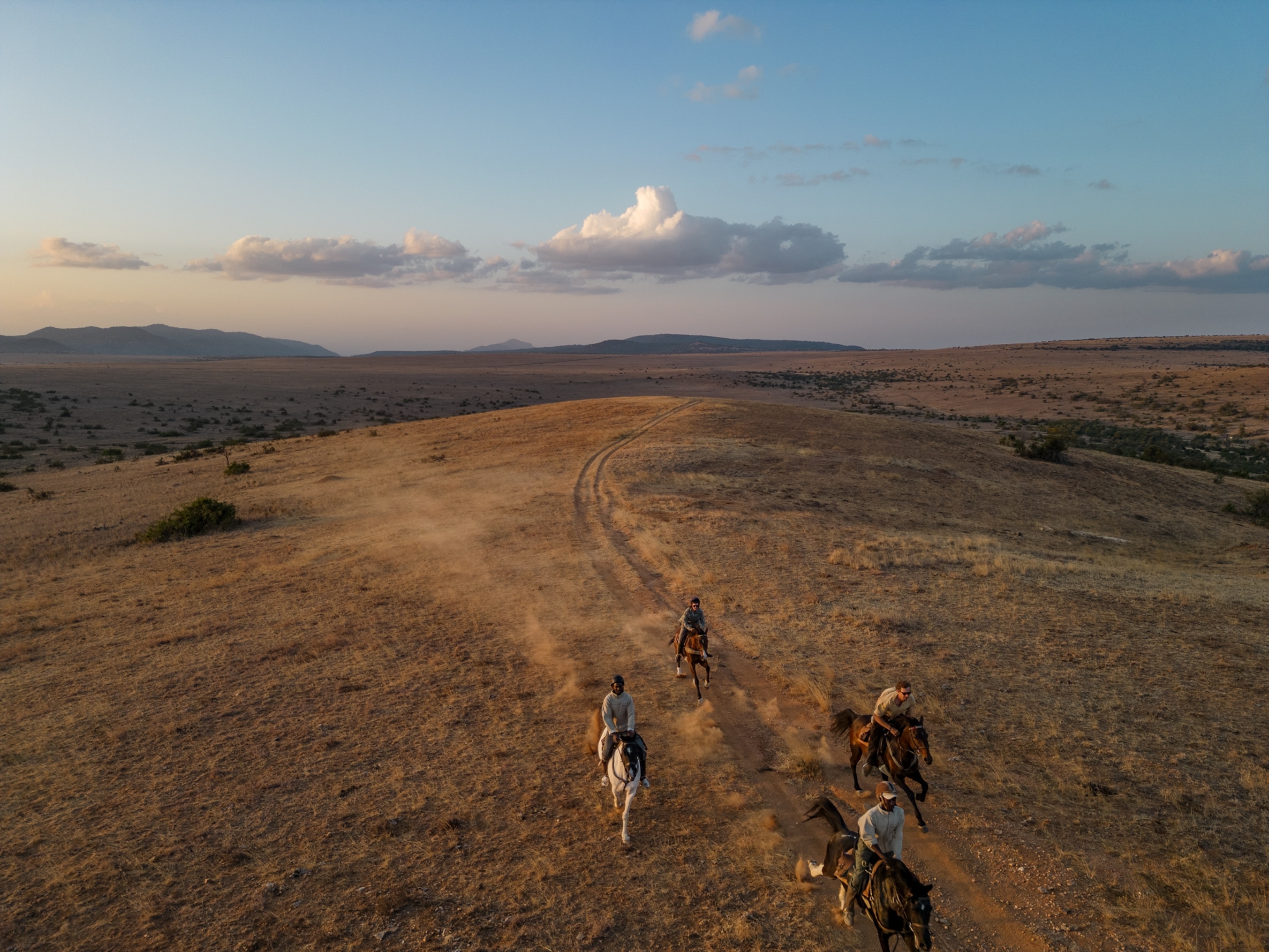 An aerial view of riders galloping over a hill in Borana Conservancy, Kenya