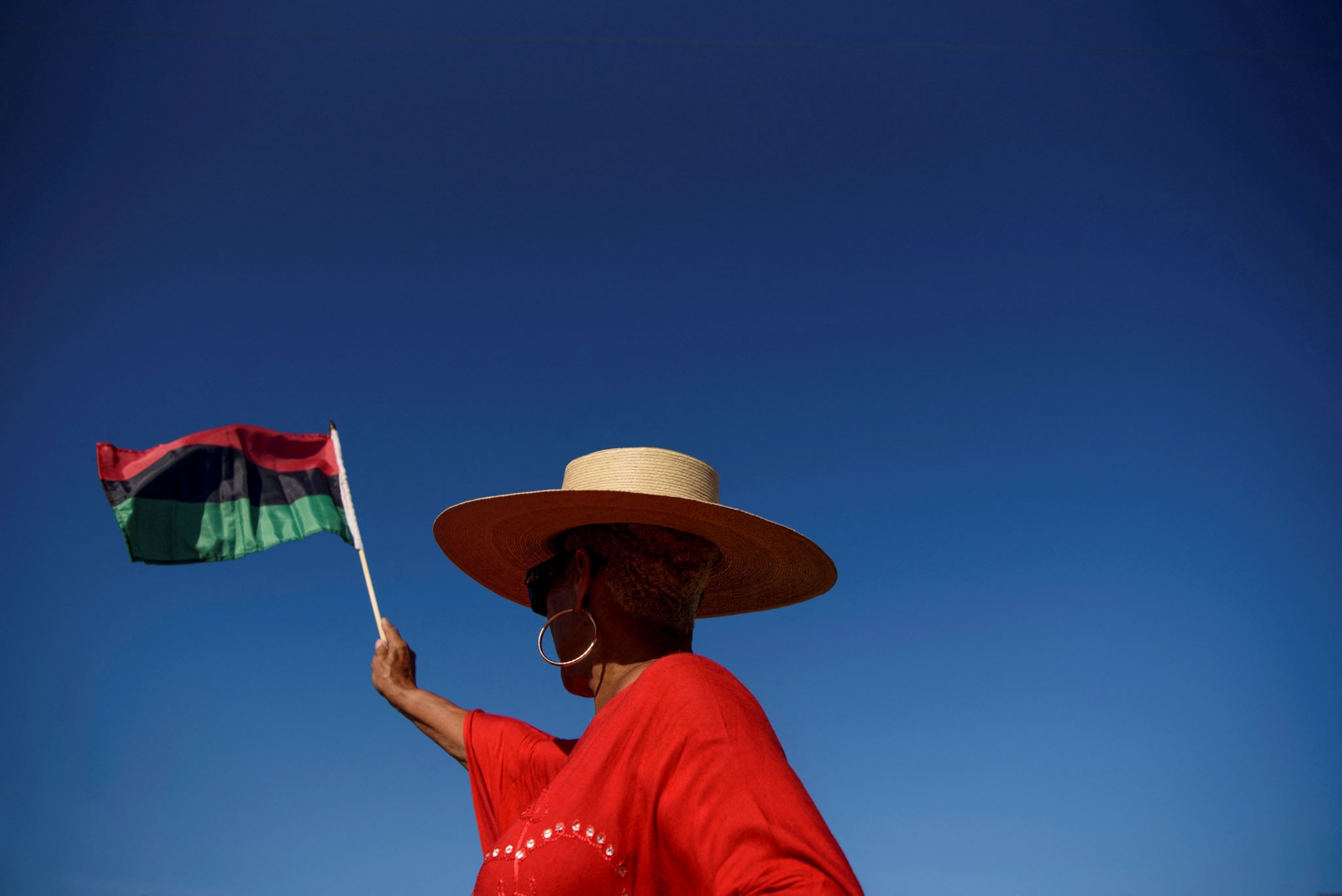 a woman wearing a full brimmed hat waves the Pan-African flag