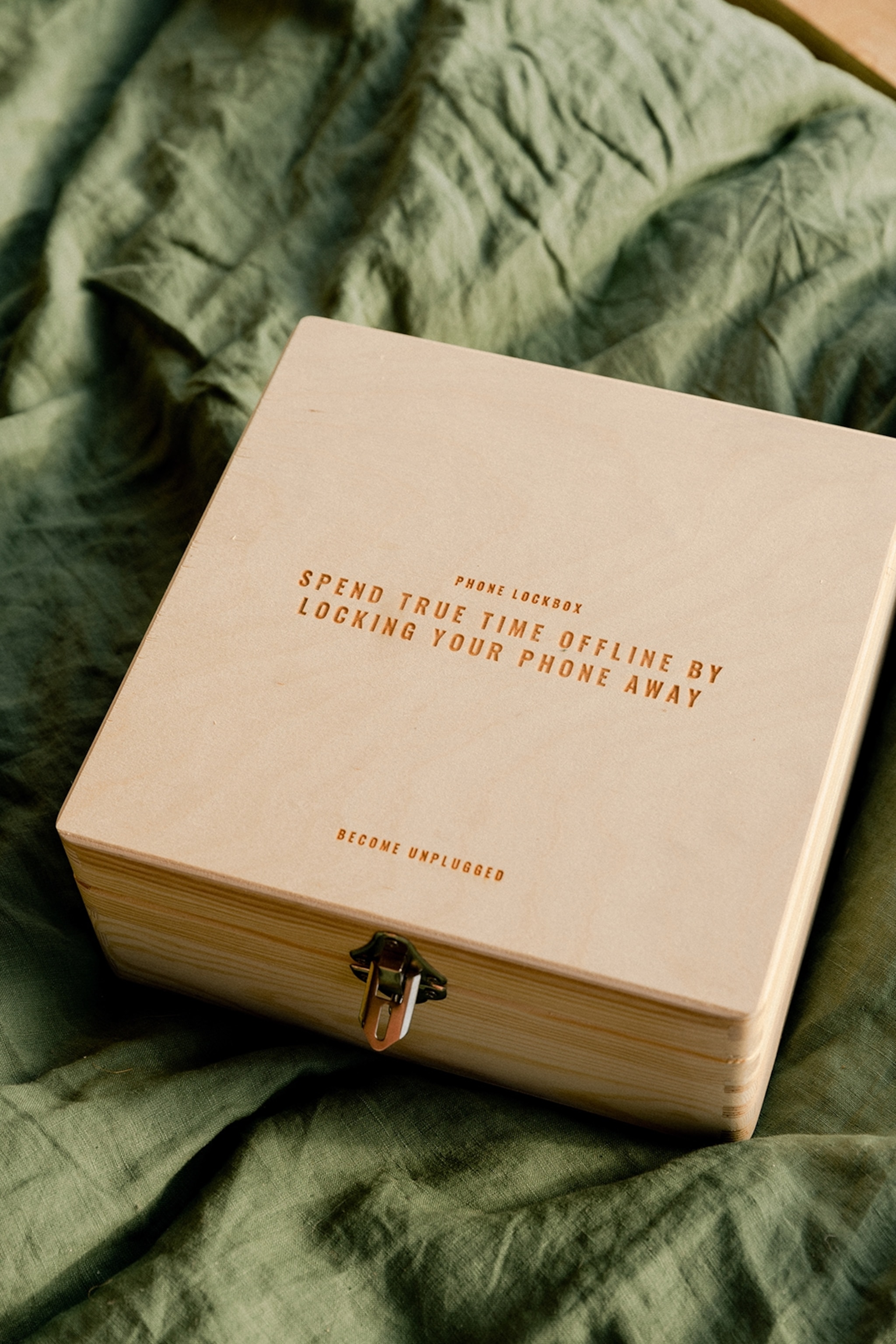 A wooden box to lock your phone in resting on linen sheets, the cover advising to spend true time offline.
