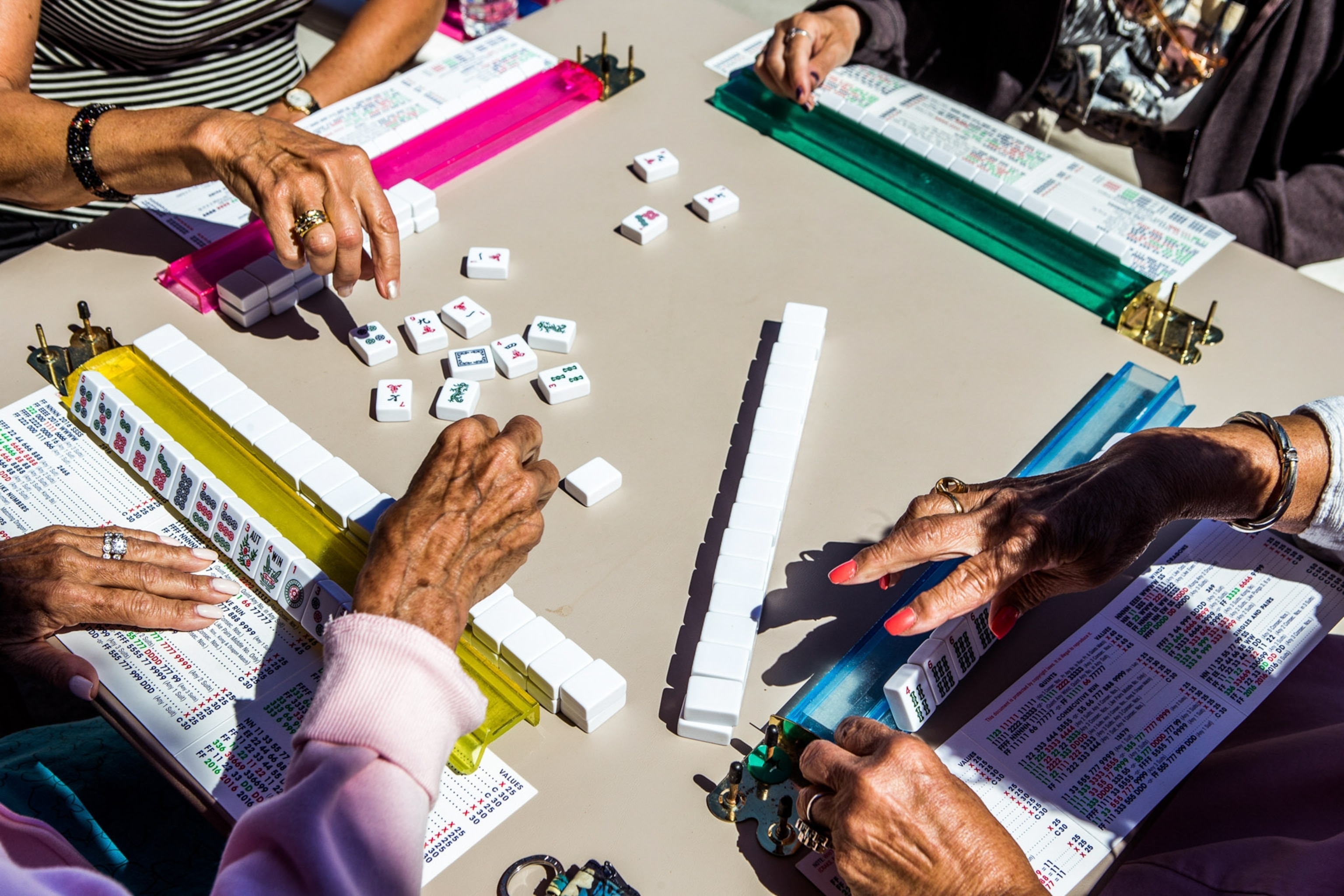 Hands above a mahjong table with tiles spread out.