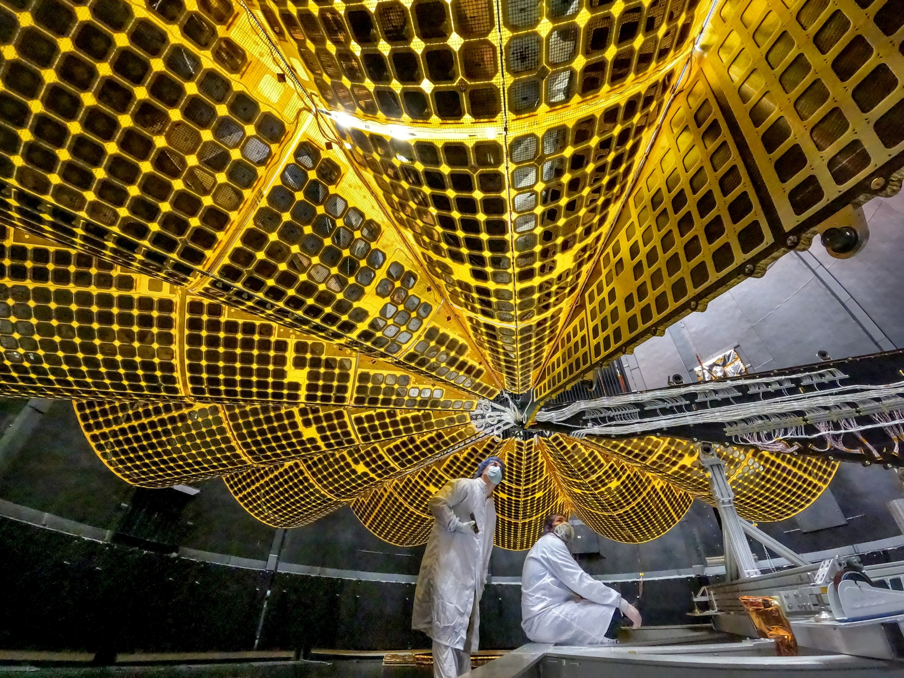 Picture of two persons in white lab coats and face masks under golden umbrella.
