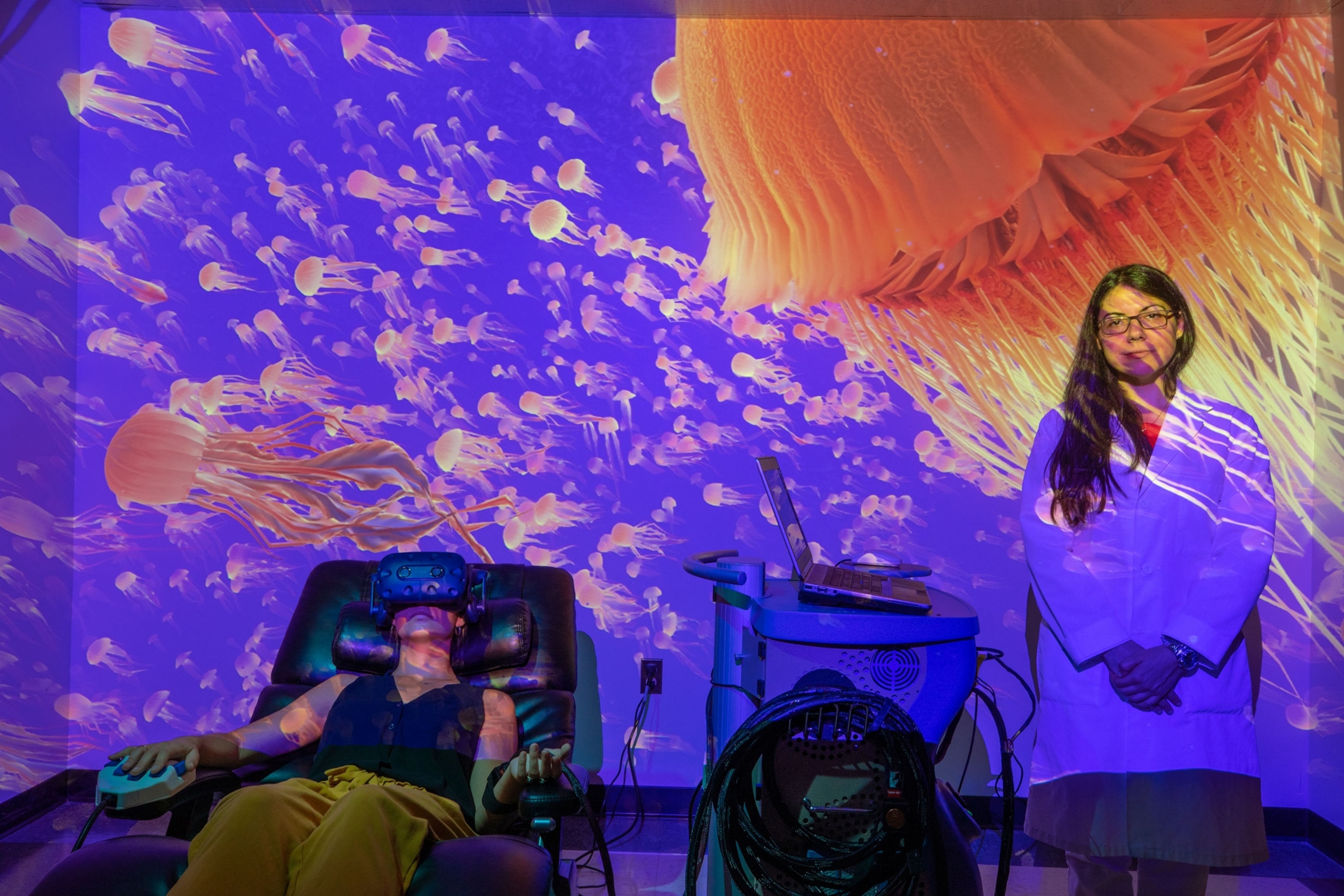 woman standing and another person in goggles in chair with a marine life on background.