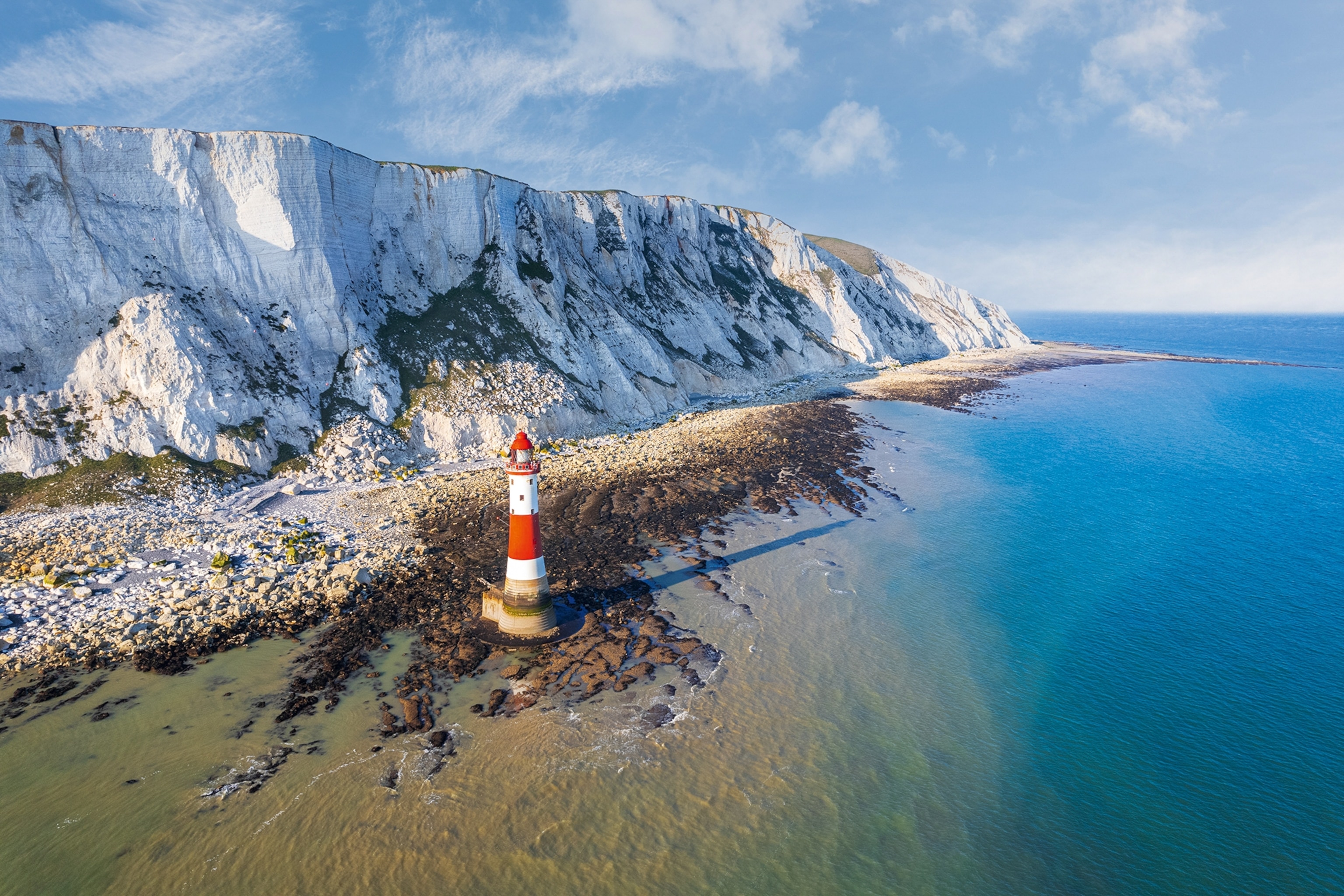 White cliffs stretching out into the sea with a red and white painted lighthouse on the shore