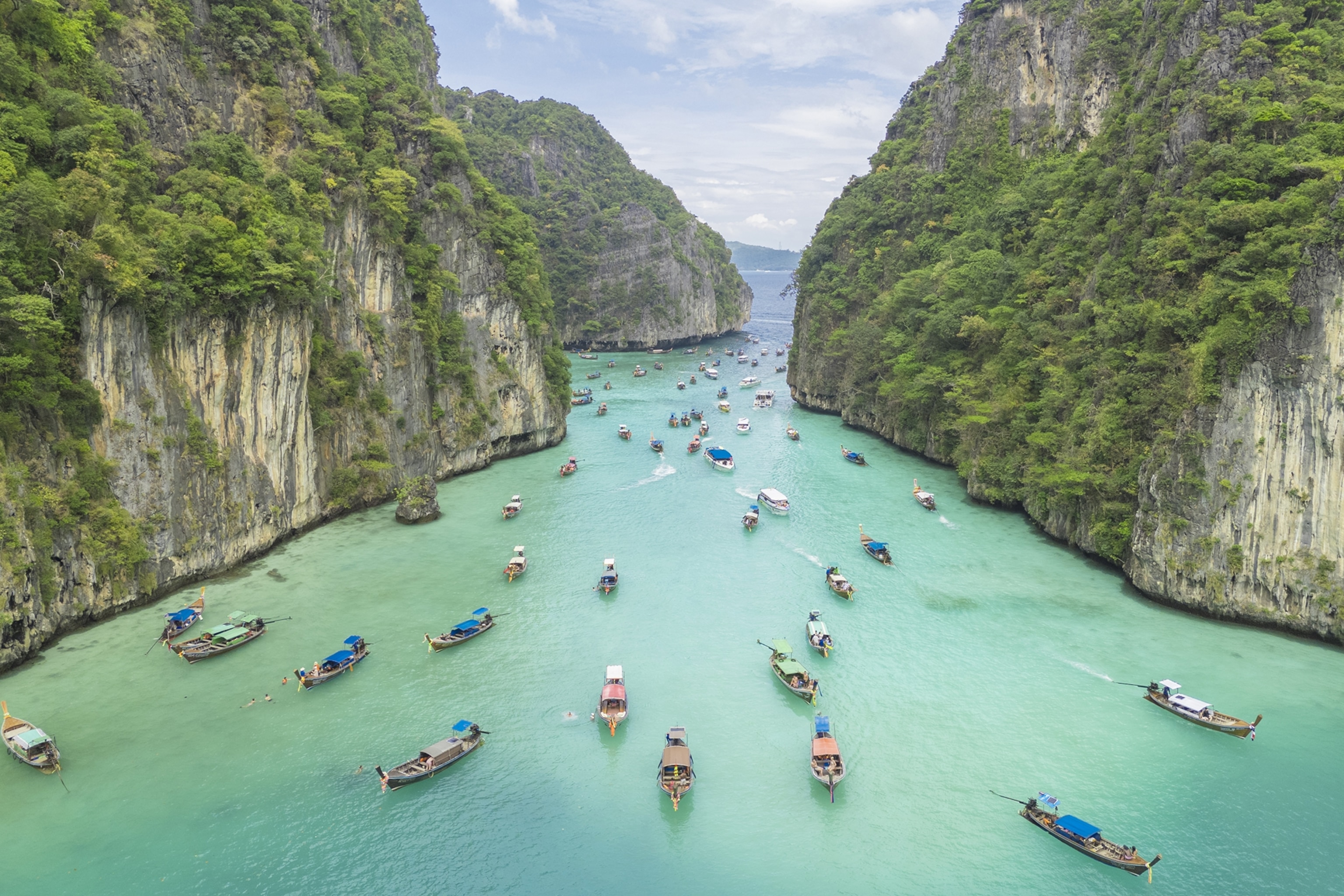 A birds-eye view on a cliff-hugged bay with small boats dotted around the sea.