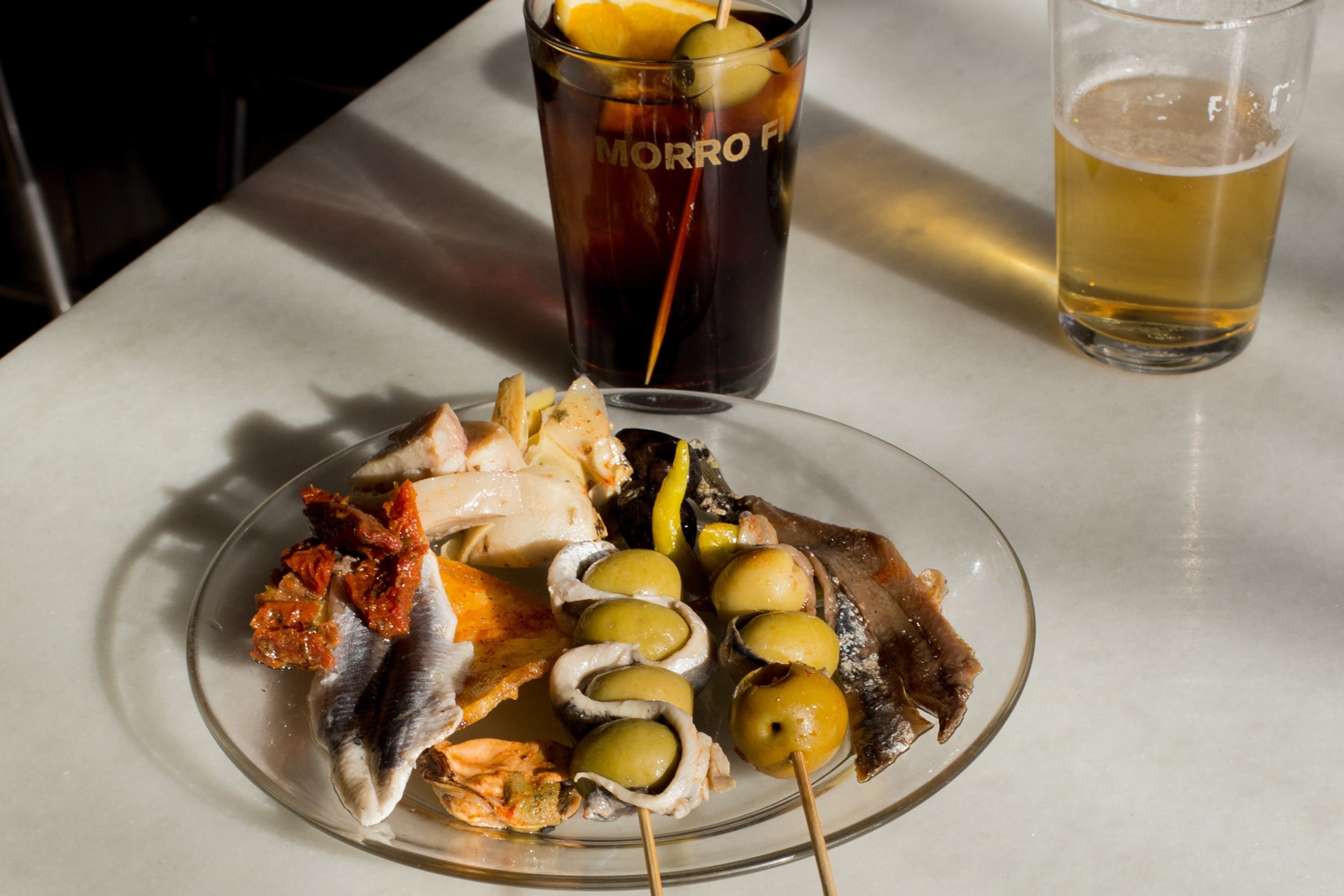 A plate of anchovies, artichokes and olives, with a vermouth drink.