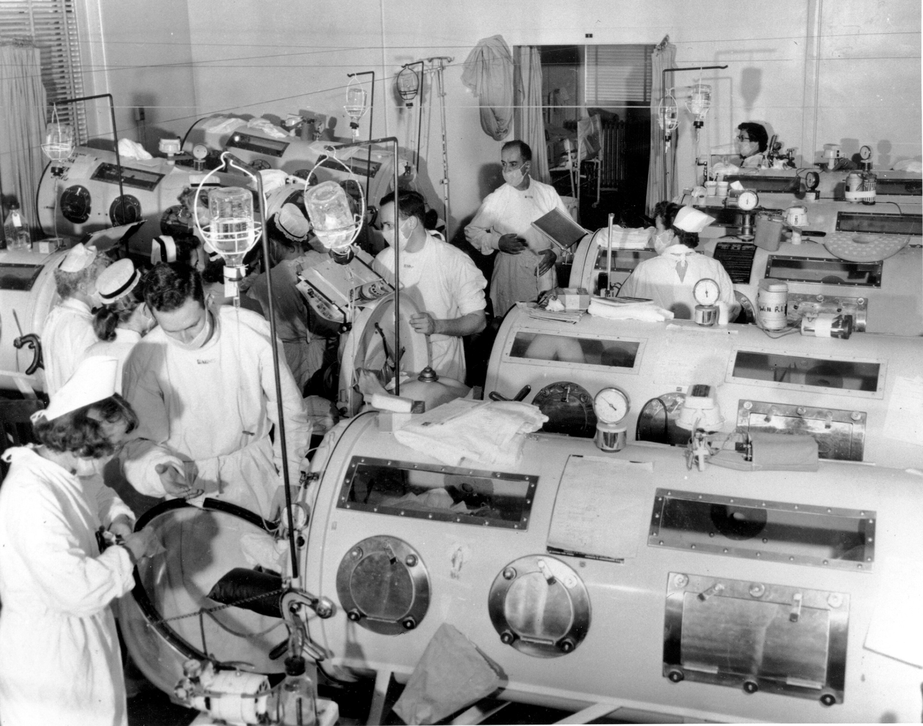 historical black and white photo of medical team around metal cases with glass windows.