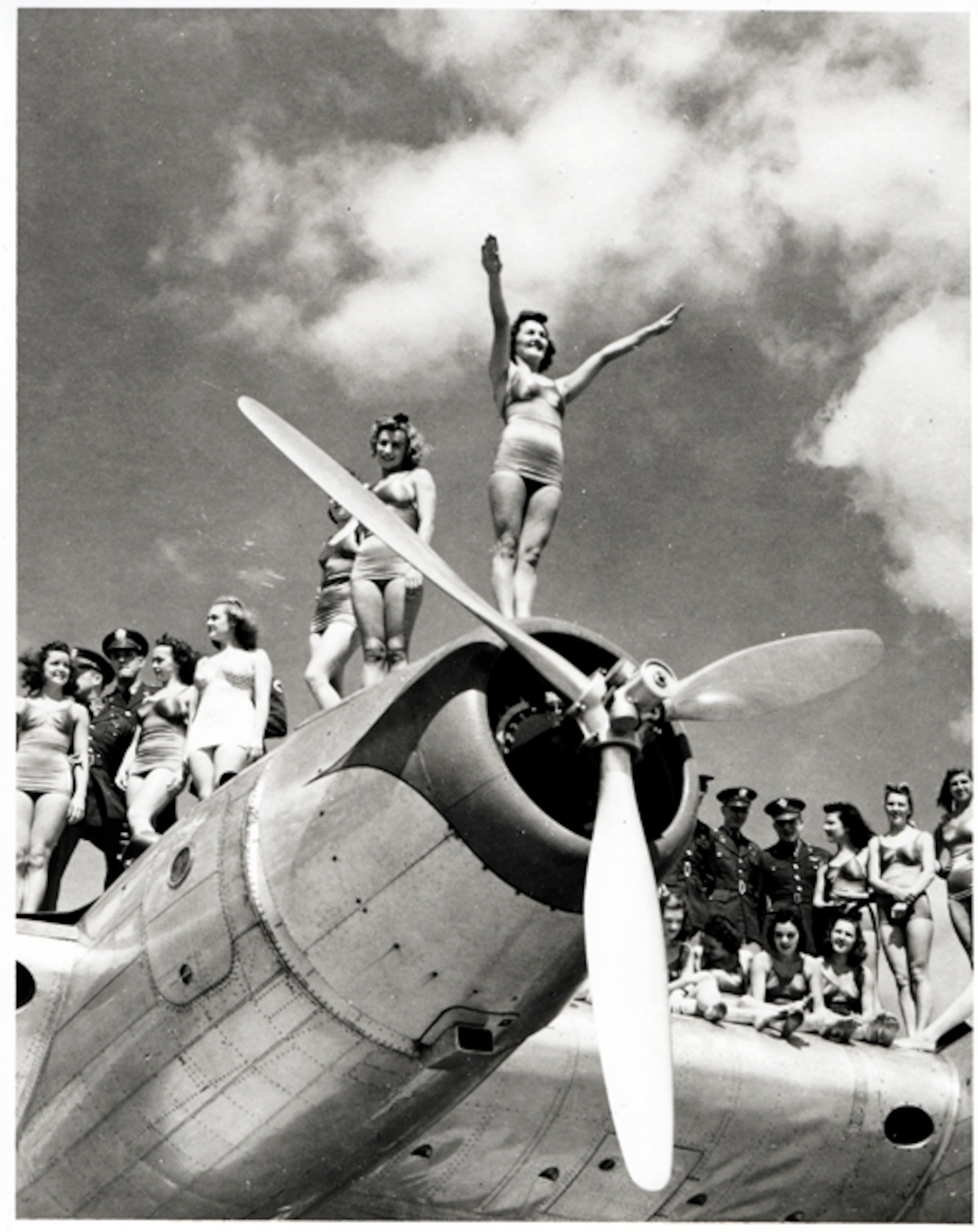 women in swimsuits next to soldiers on top of a World War II bomber.
