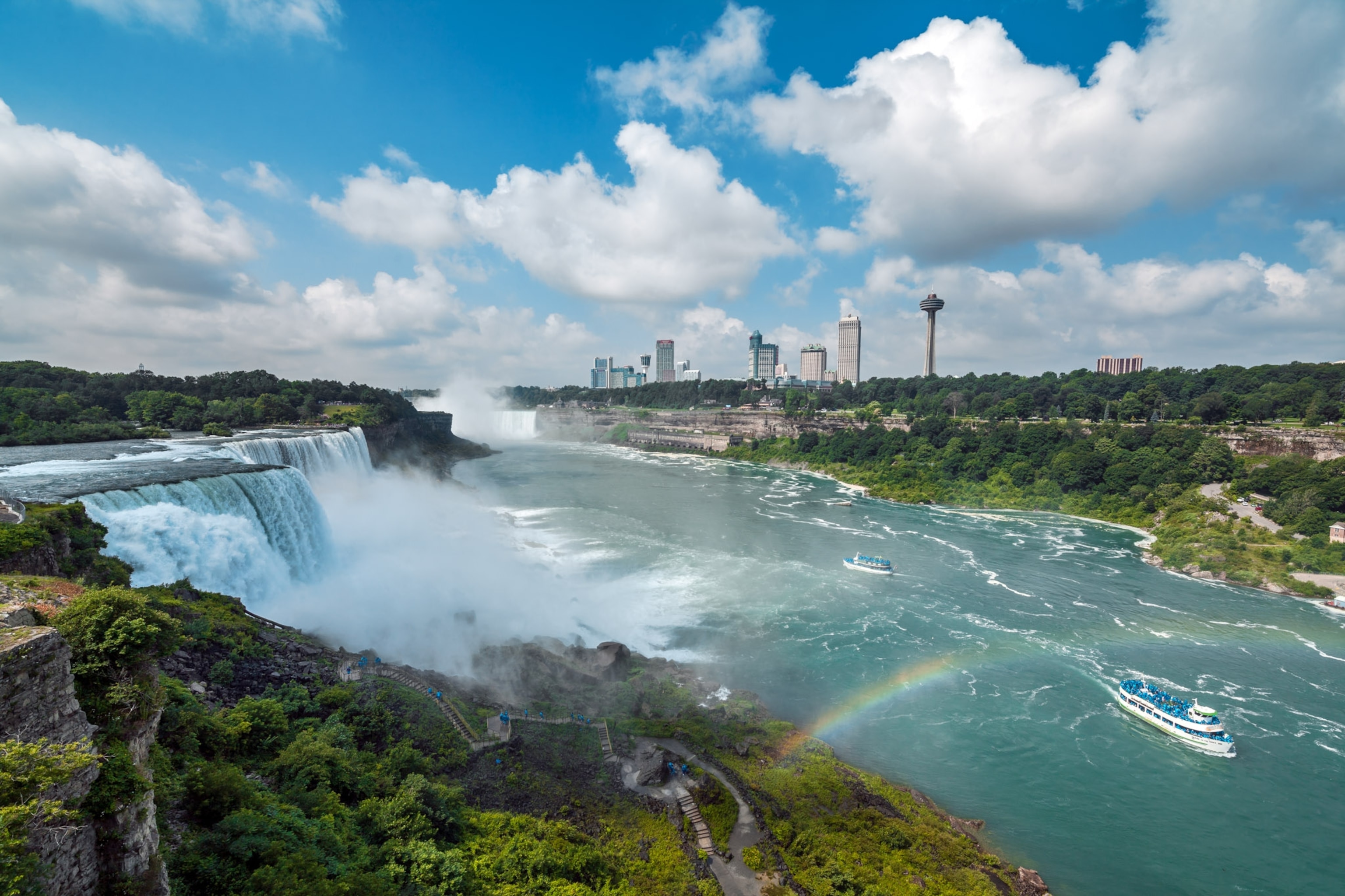 Blue water gushes from the falls with a rainbow in the foreground.