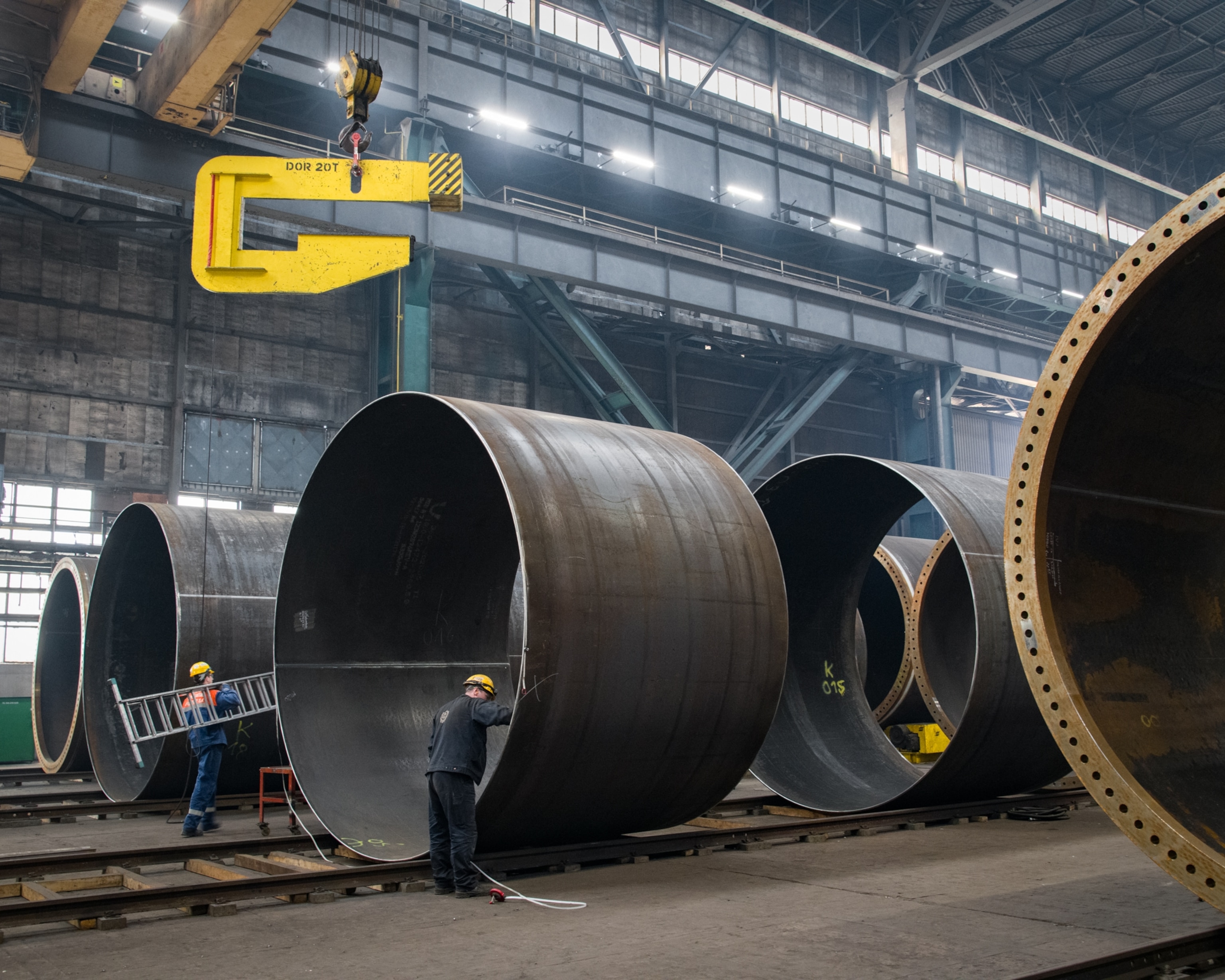 a few workers standing within large metal cylinders used at the shipyard
