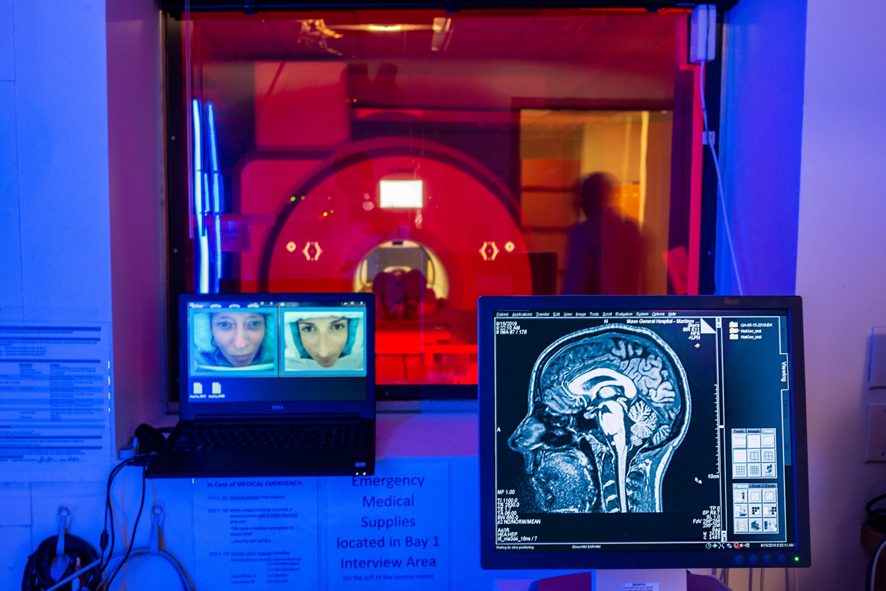scanner room in red light on background and two monitors glowing blue on foreground.