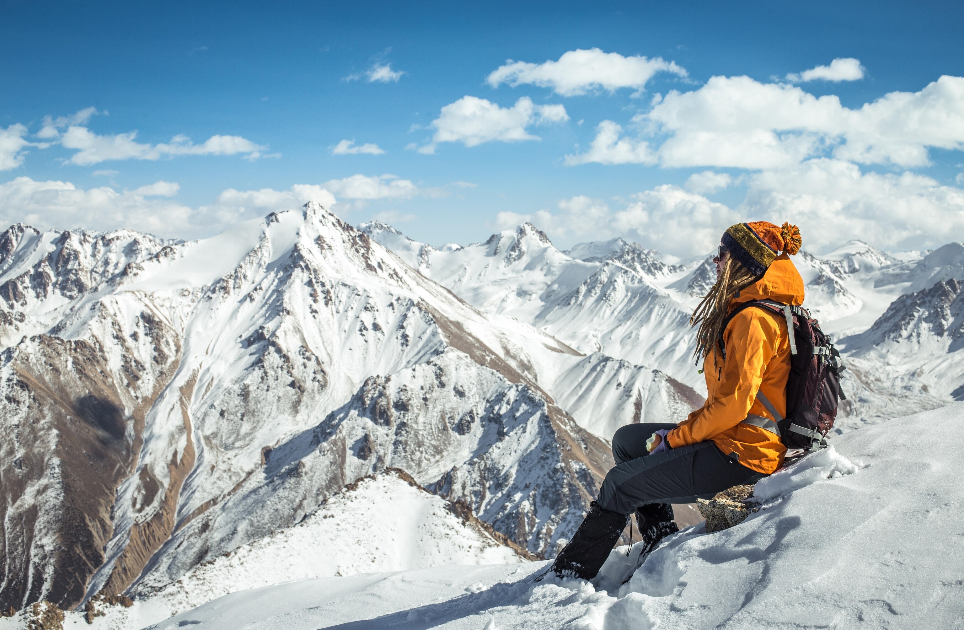 Outdoor girl is sitting on the top of mountain and enjoying the view on surroundings snow peaks.