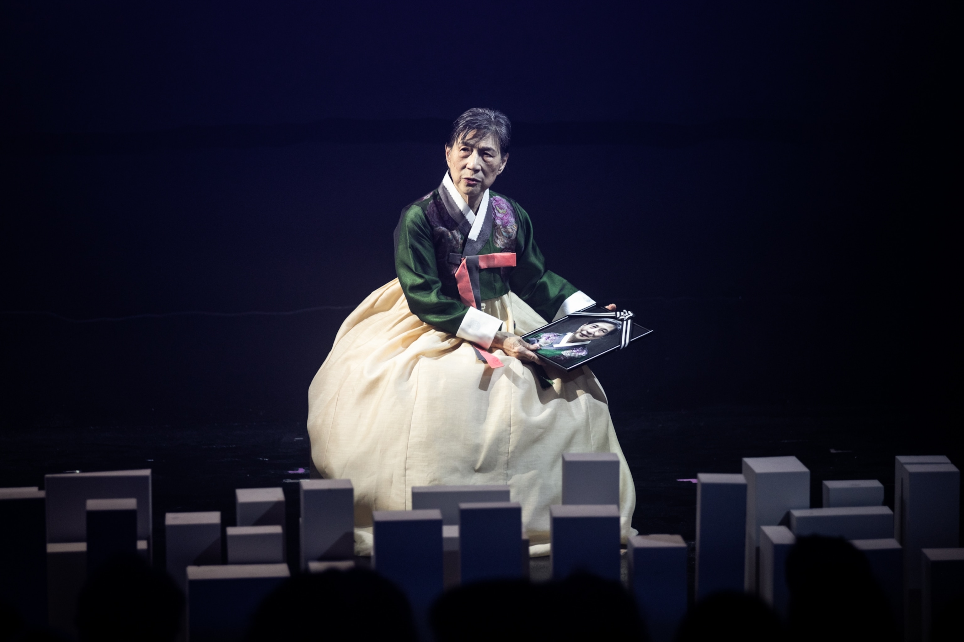 an actor in traditional asian clothing holds an old photo in a sad way