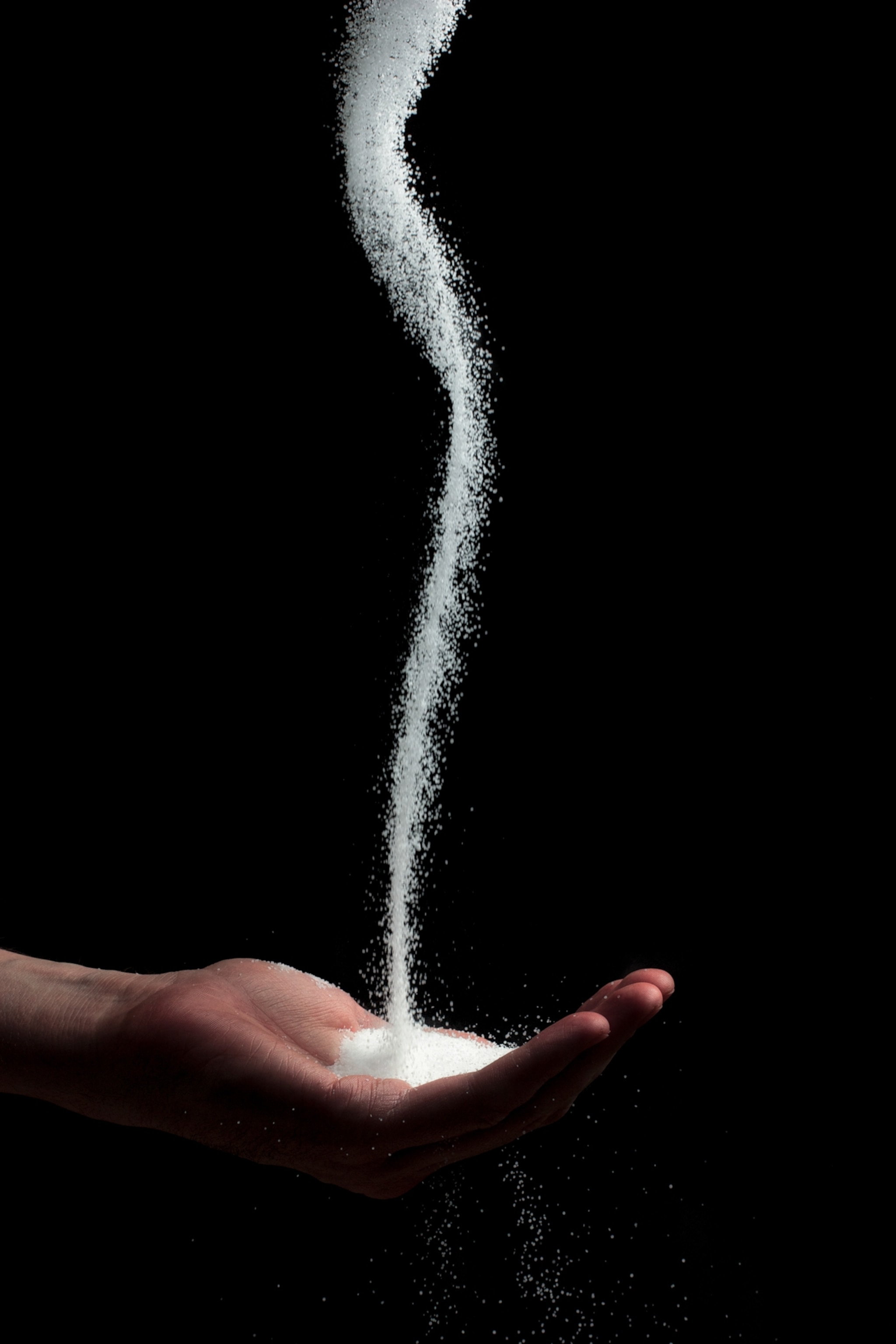A stream of salt being poured into an open palm, photographed against a black backdrop
