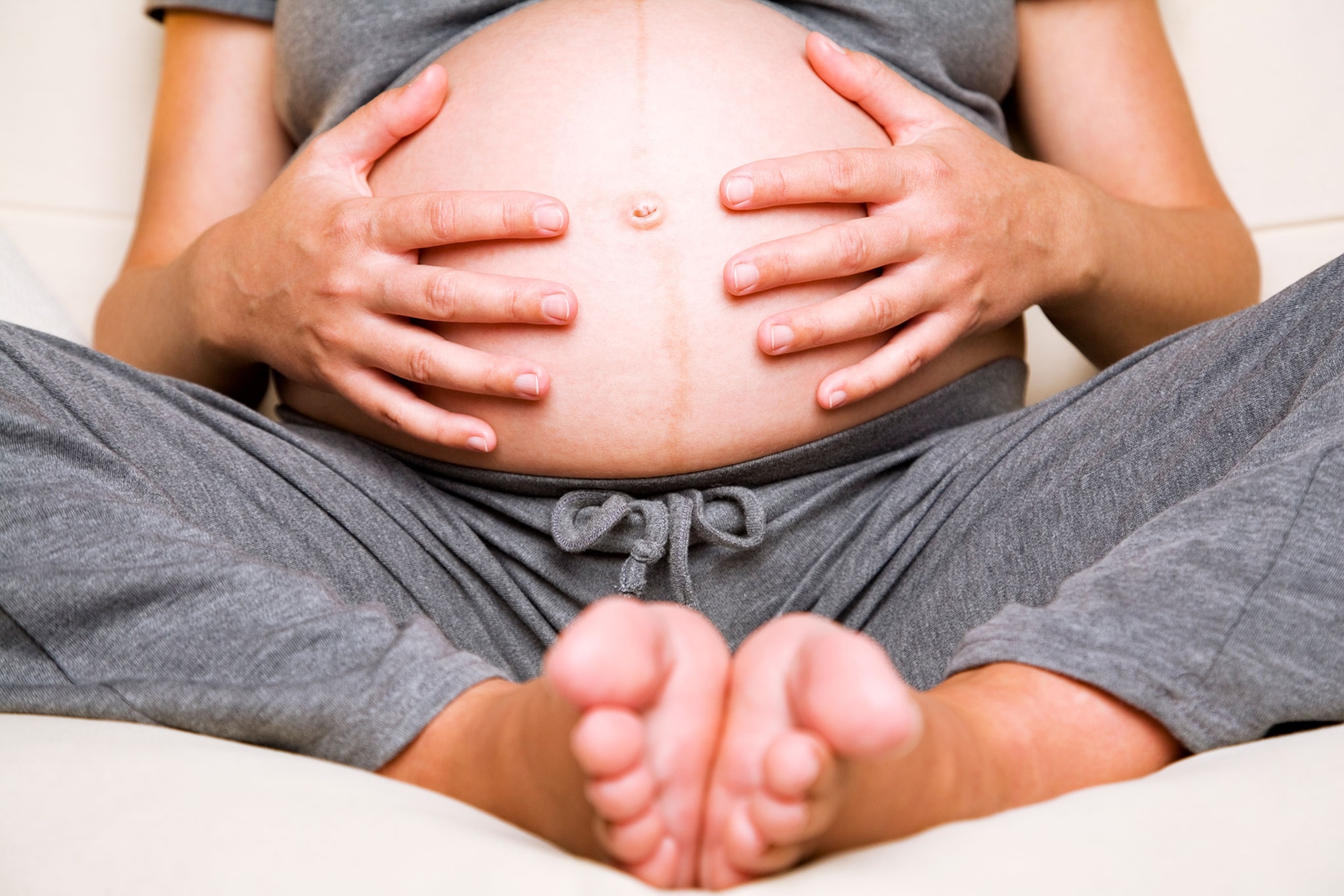 A view of a woman's feet and her hands holding her pregnant stomach.