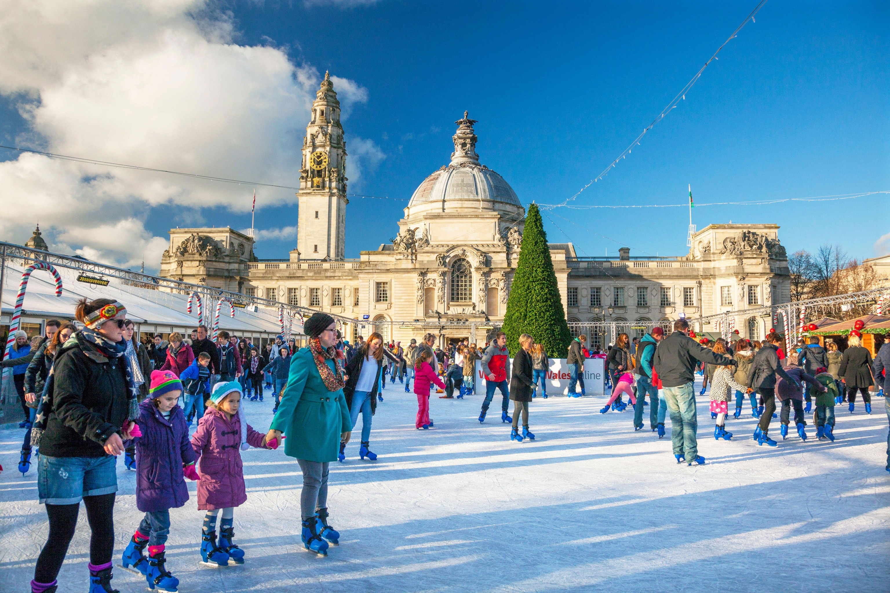 families skating on ice rink in front of castle with clear blue skies overhead
