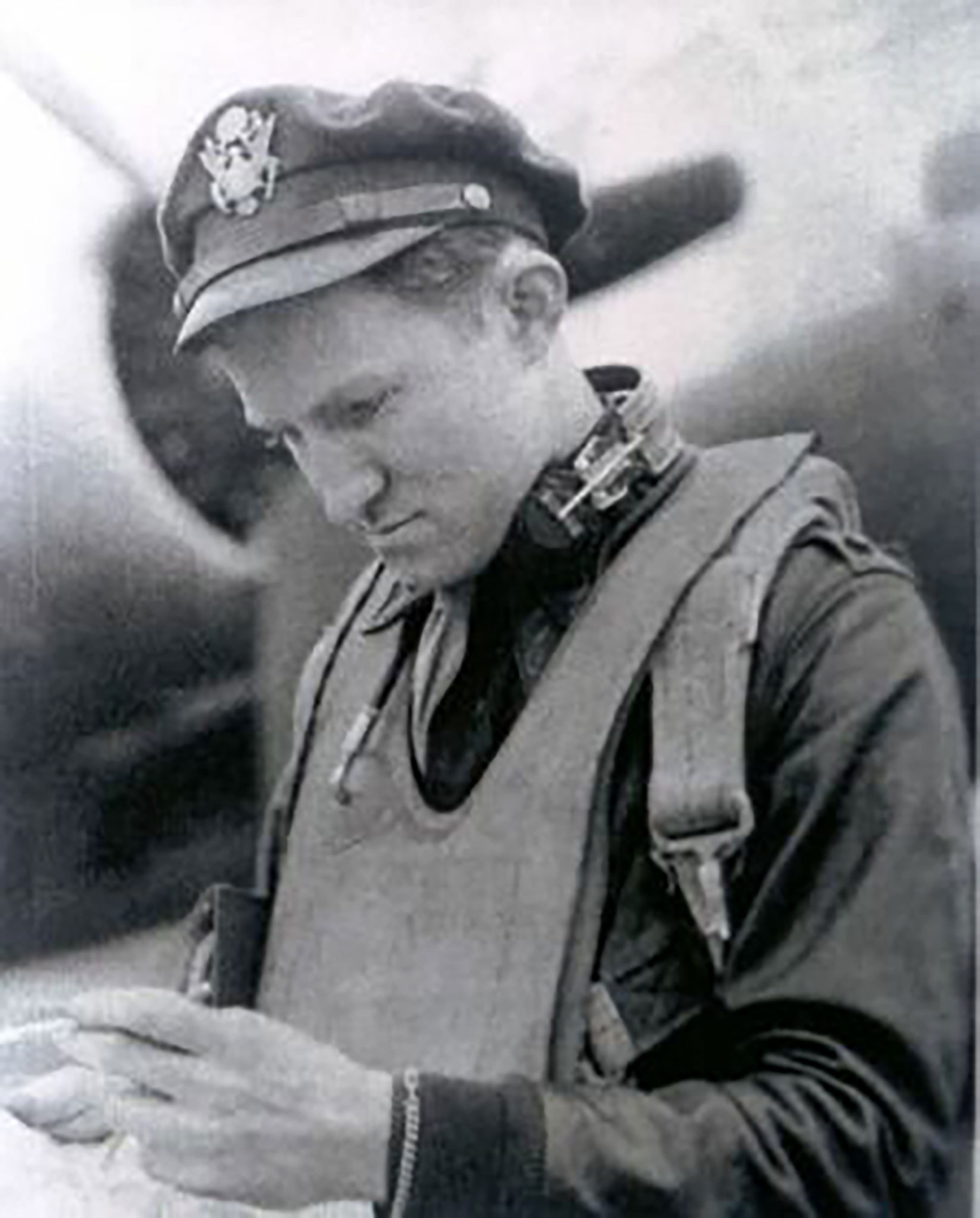 MAJOR H. H. CROSBY (Anthony Boyle). A black and white photo depicting a man in an army shirt with tie and army hat looking at his hands. An uninflated life jacket hangs around his neck.