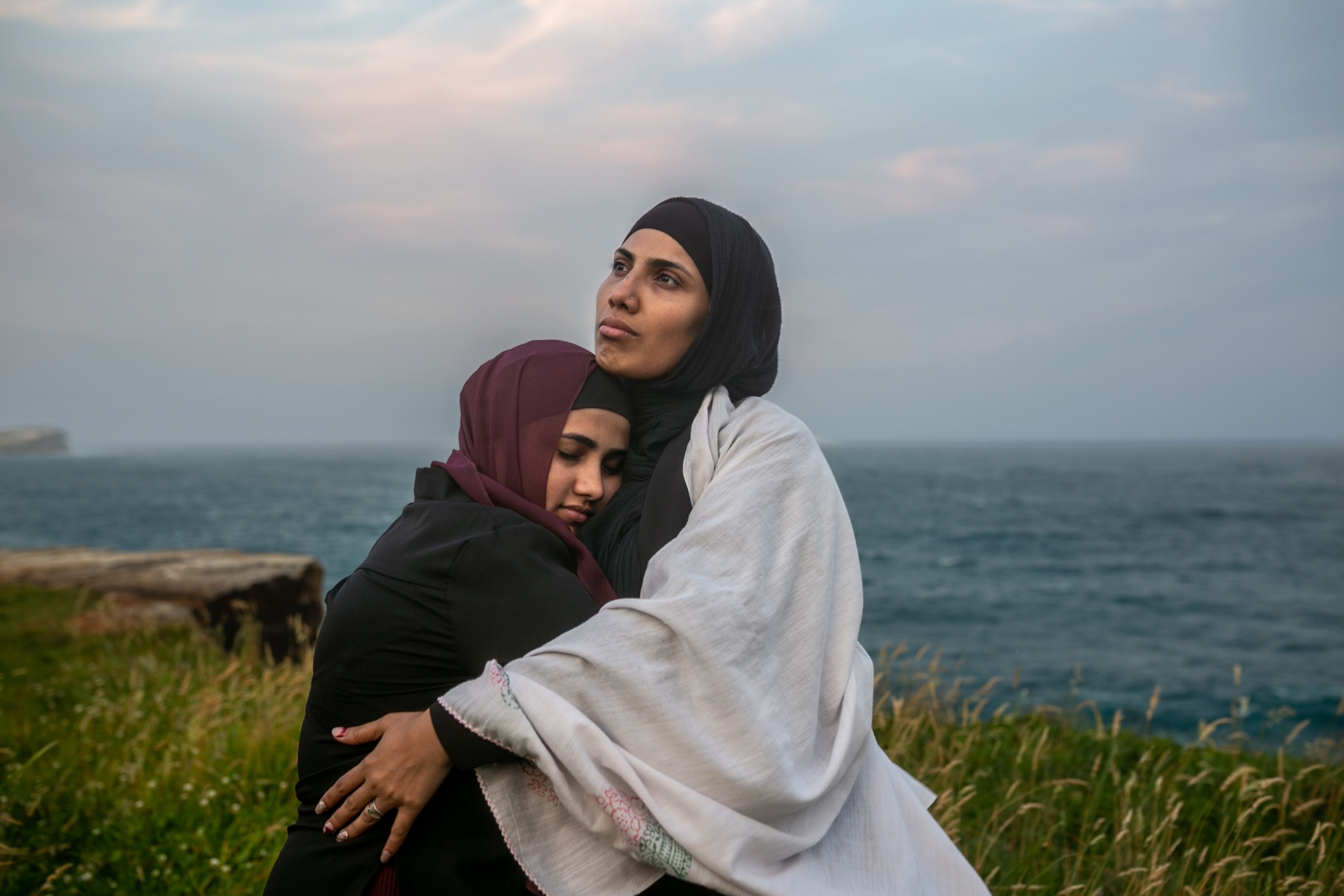 a woman hugging another woman while standing on a coastline