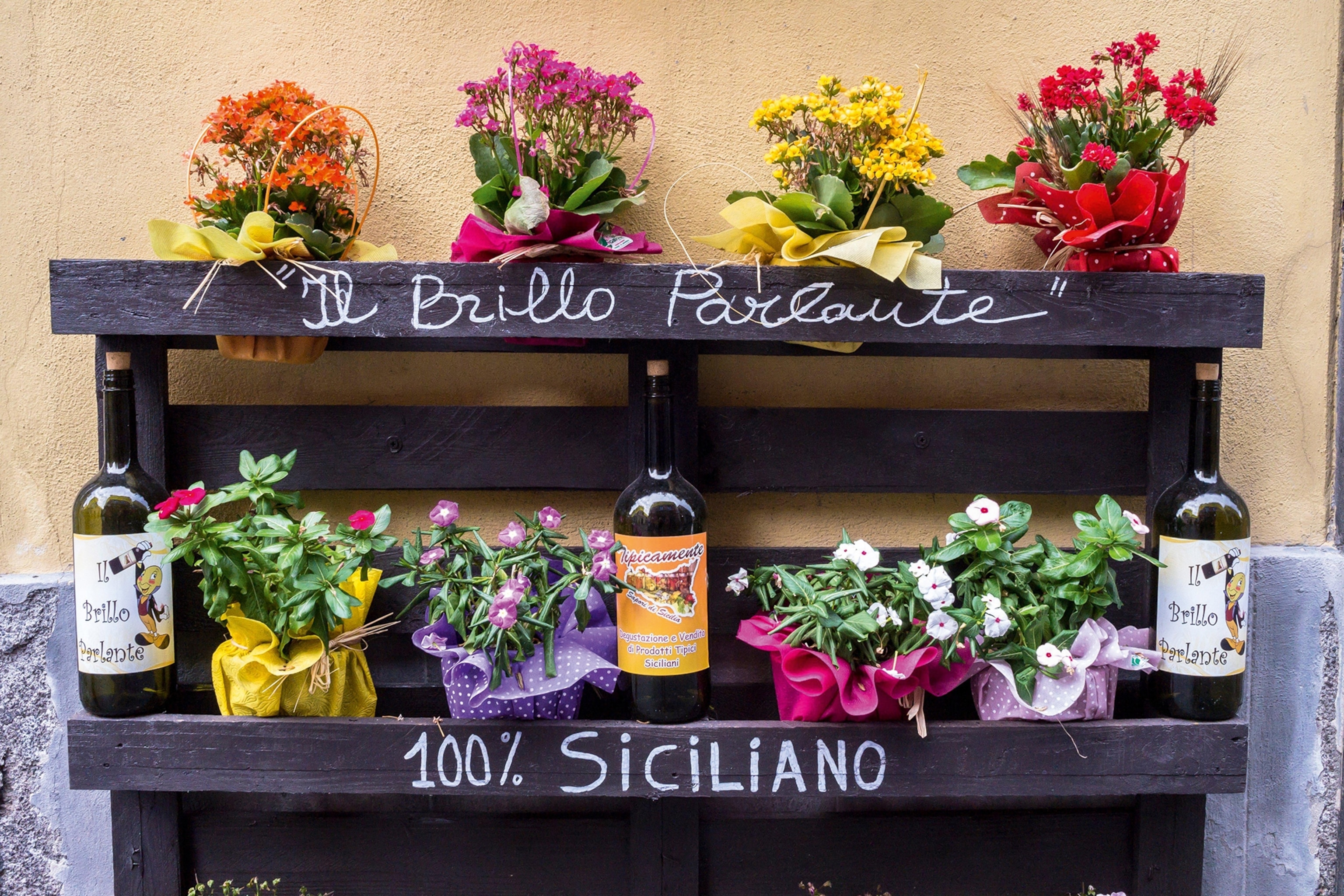Shelves of flower baskets and wine bottles. 100% Siciliano is written on the shelves.