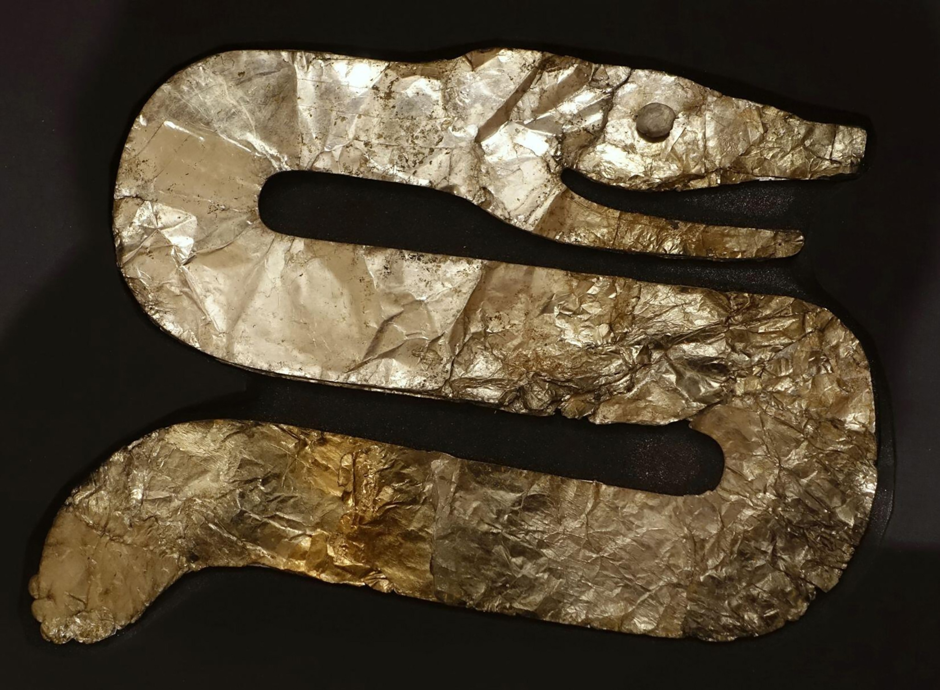 A gold colored serpent effigy from the Hopewell Culture against a black background.