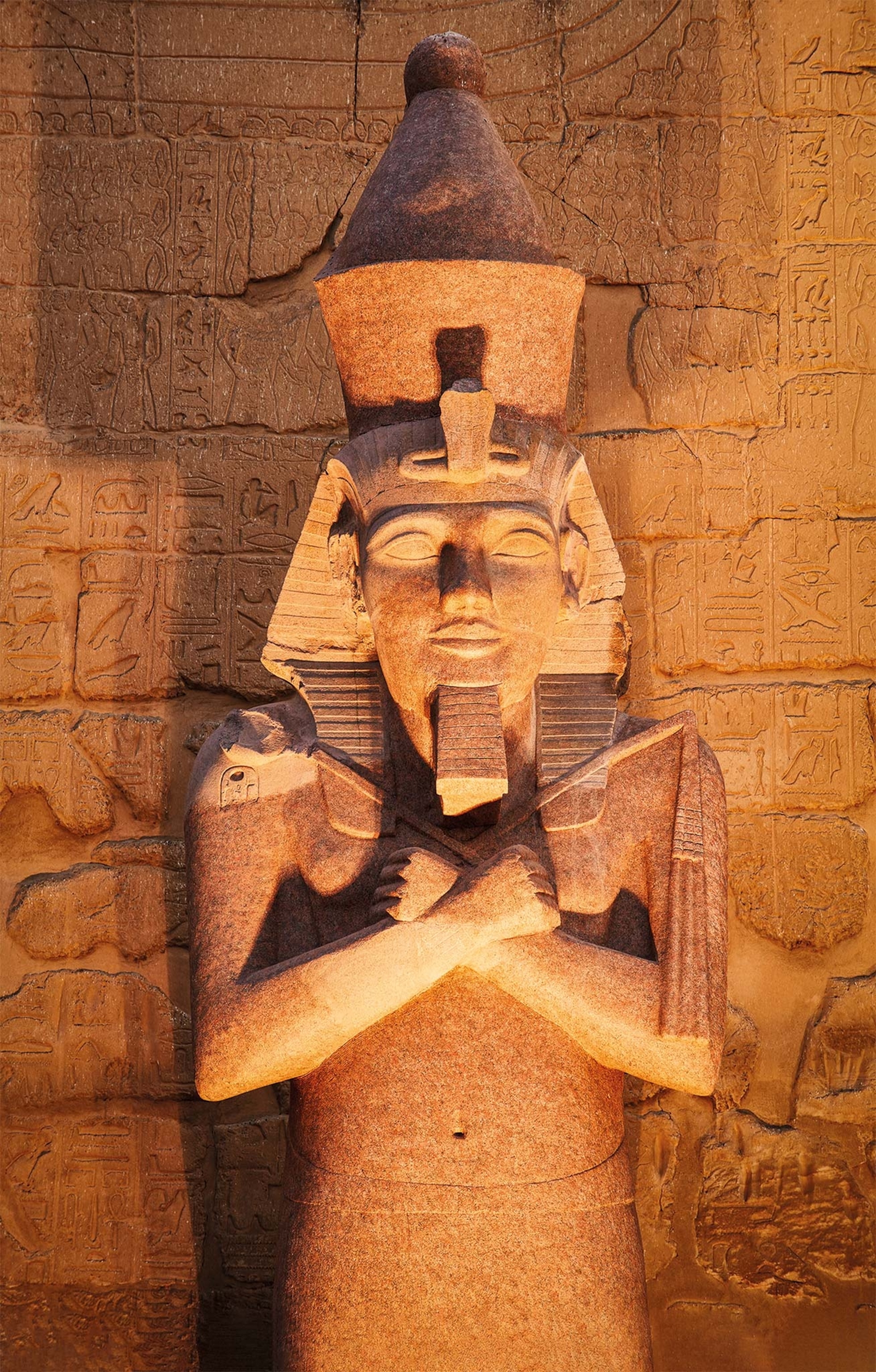 A colossus of Ramses II stands before the Temple of Luxor. He wears the double crown and wields a scepter and staff.