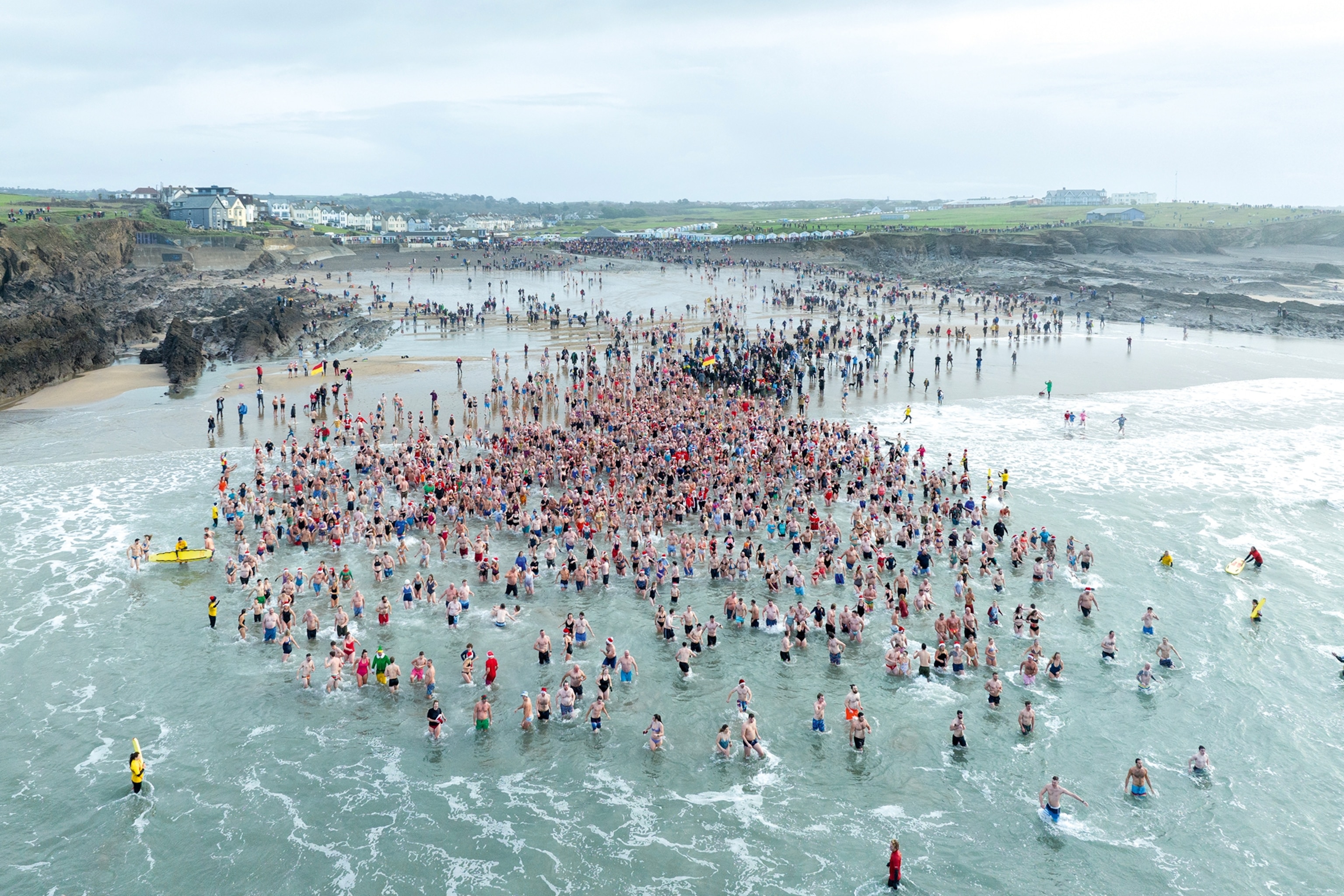 A group of swimmers in the ocean in Cornwall. They are spread all across the beach with some further in the water.