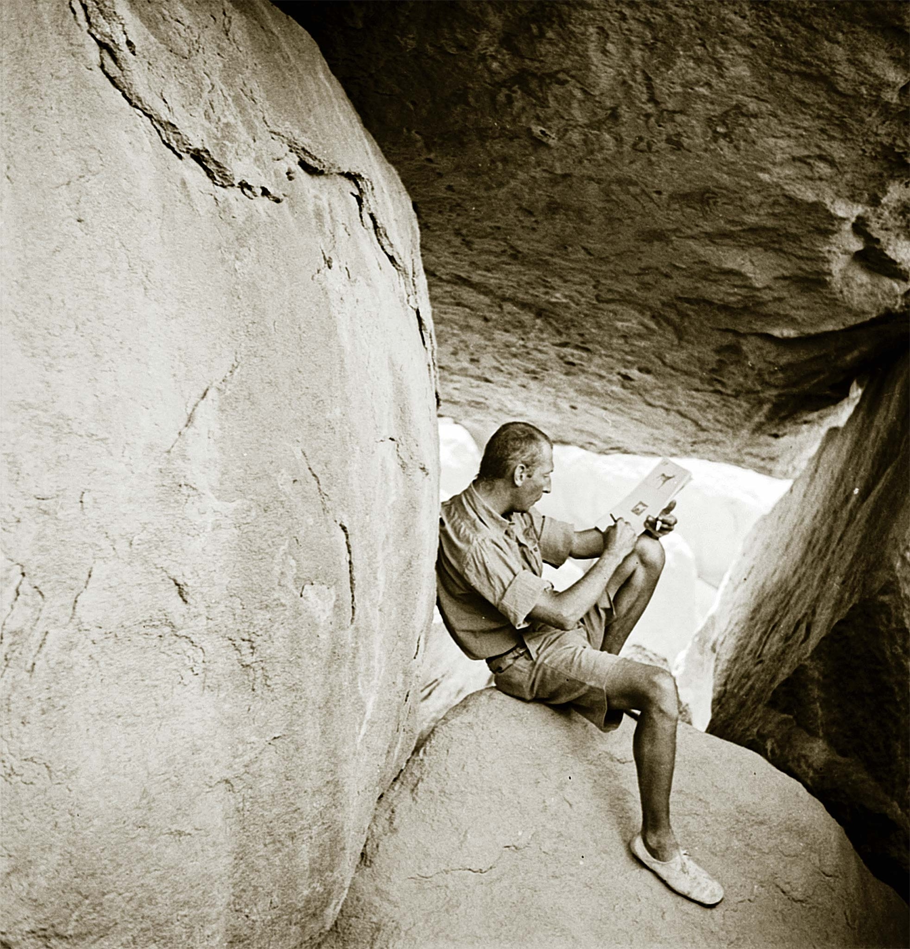 Laszlo Almásy, pictured in 1933, documents paintings found in the so-called Cave of the Swimmers while sitting on a rock.