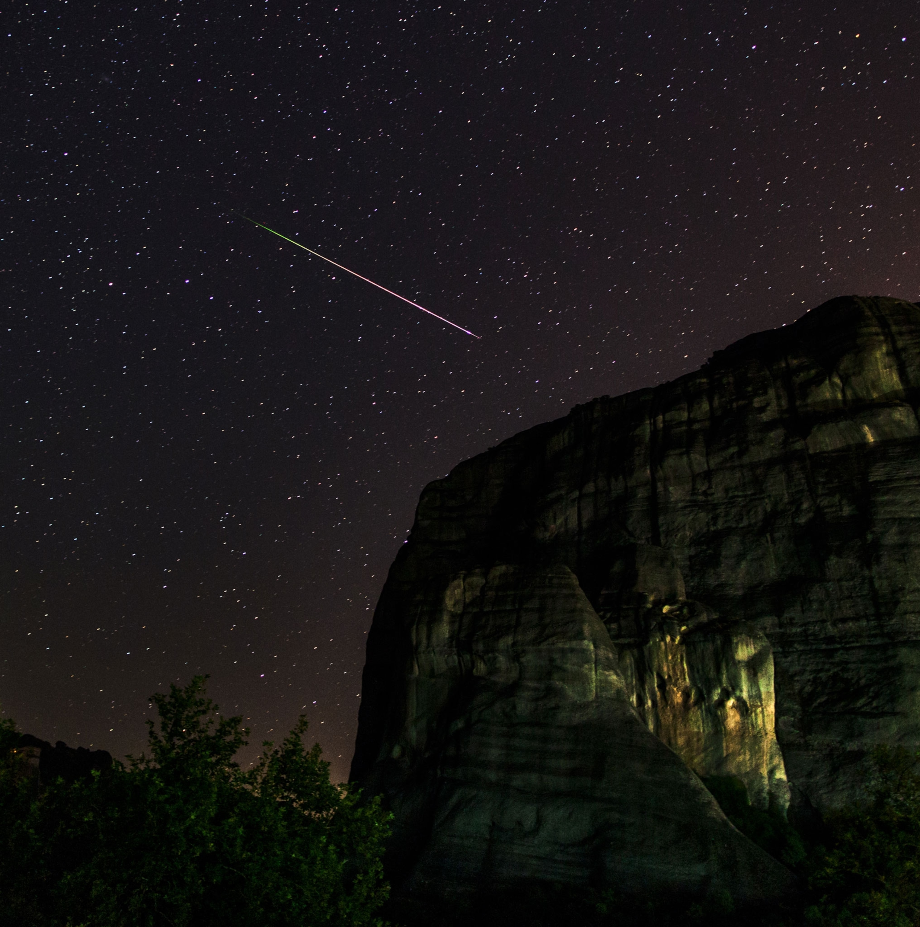 A Perseid meteor streaking across a purple starry sky over sandstone cliffs at the World Heritage Site of Meteora.