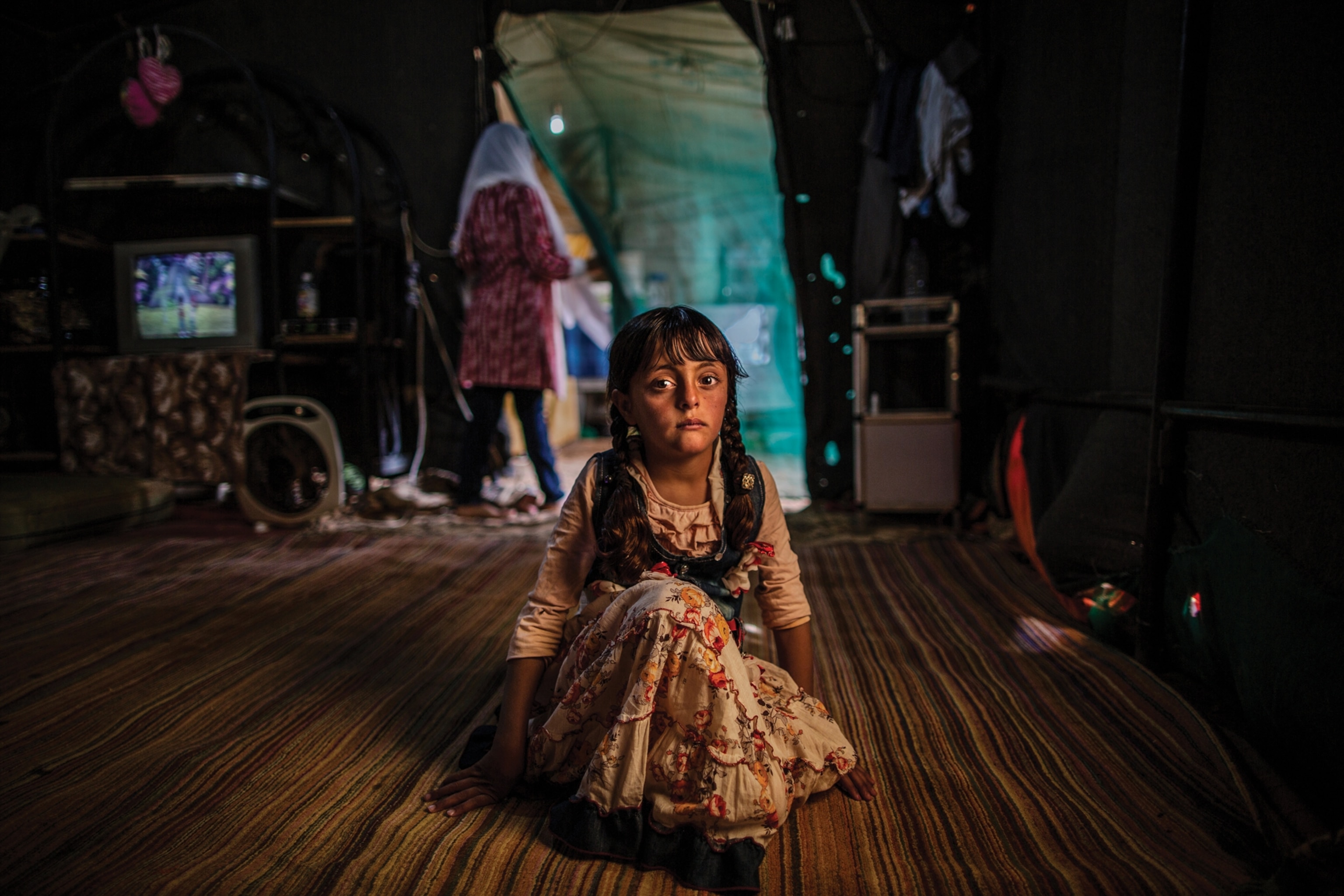 Young girl with beautiful big eyes on the floor of dark room and women in the doorway.
