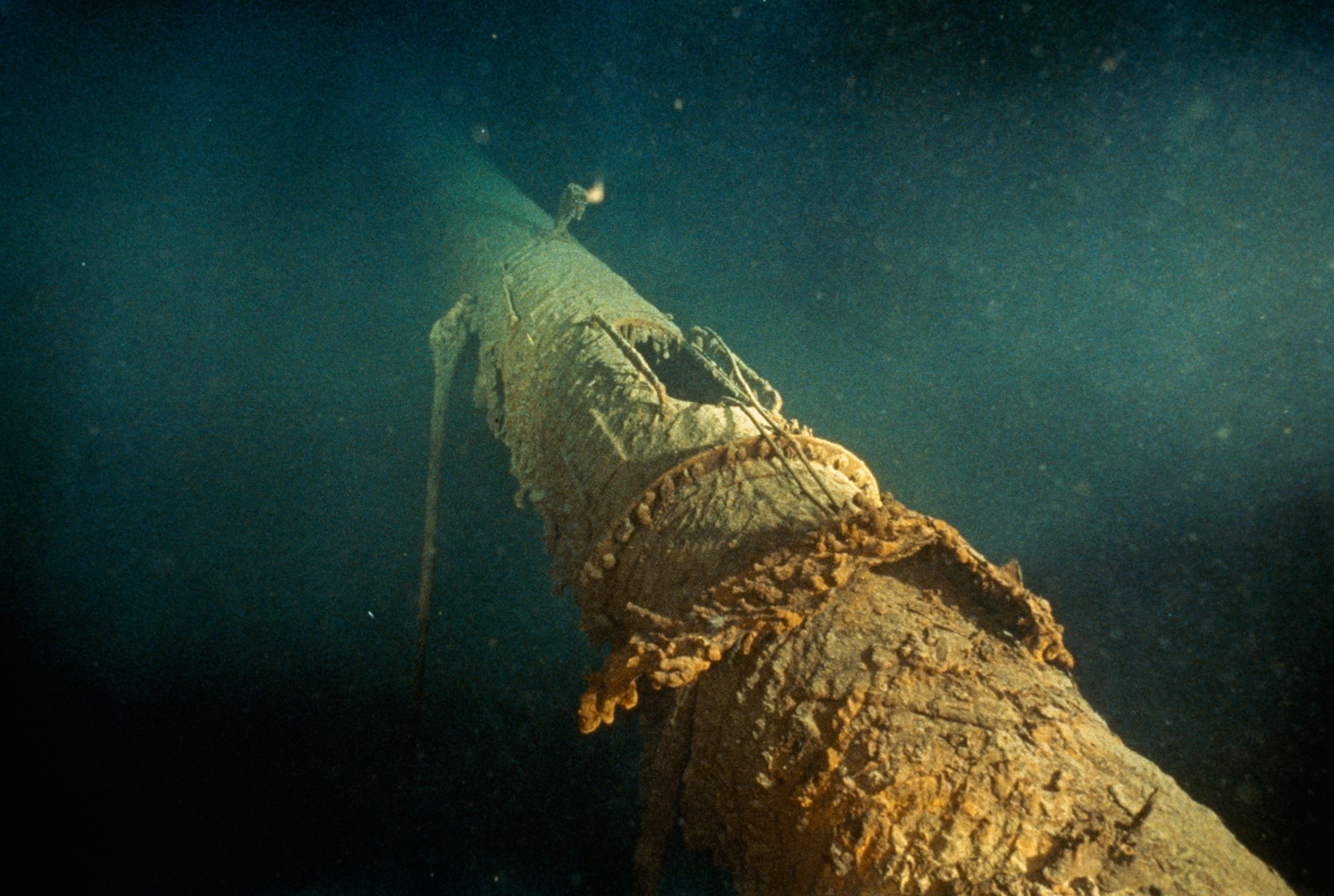 A large pipe like piece of the Titanic fallen on its side underwater and covered in elements of the ocean.