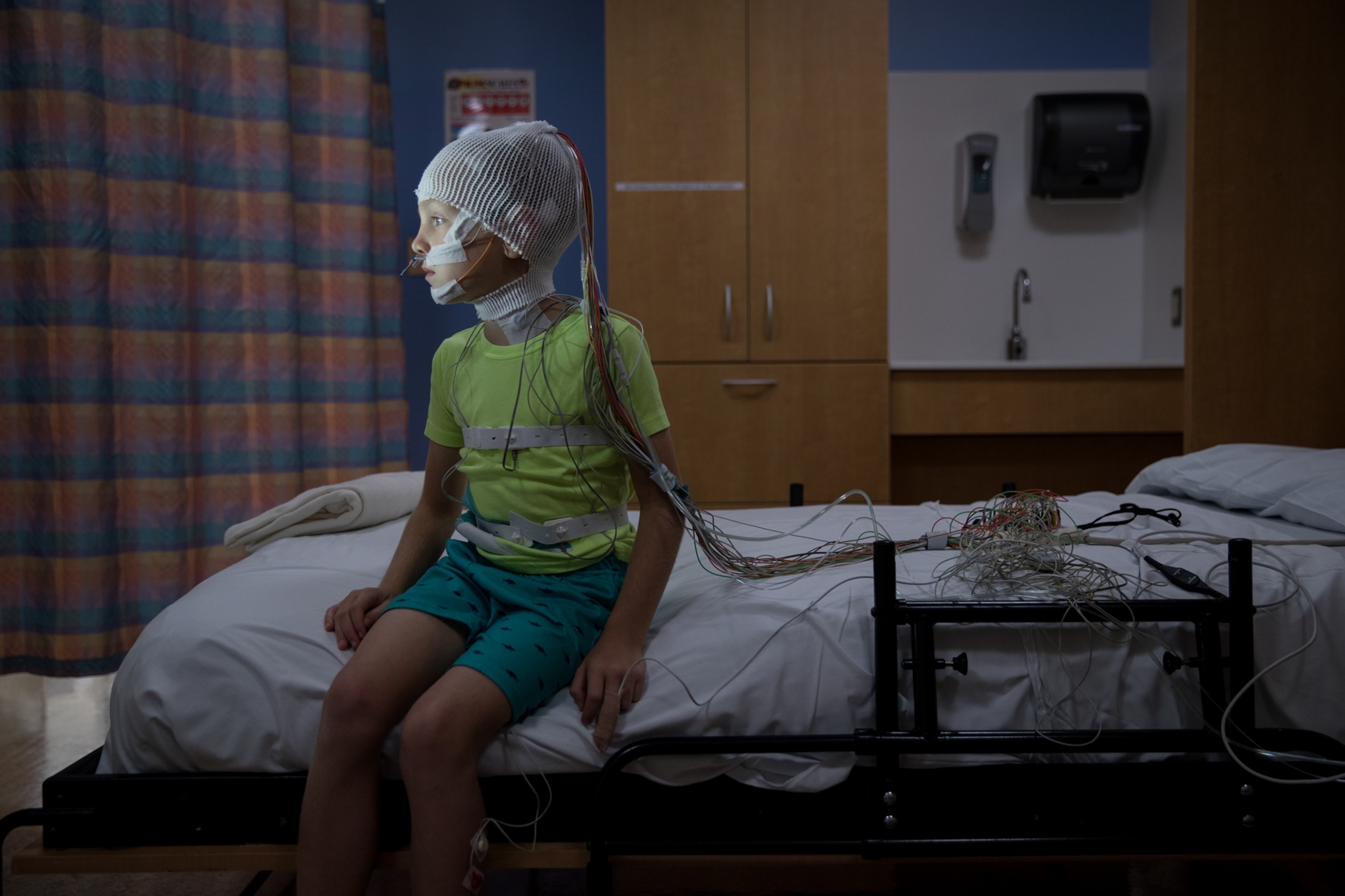 a young boy sitting in bed wearing a cap with wires