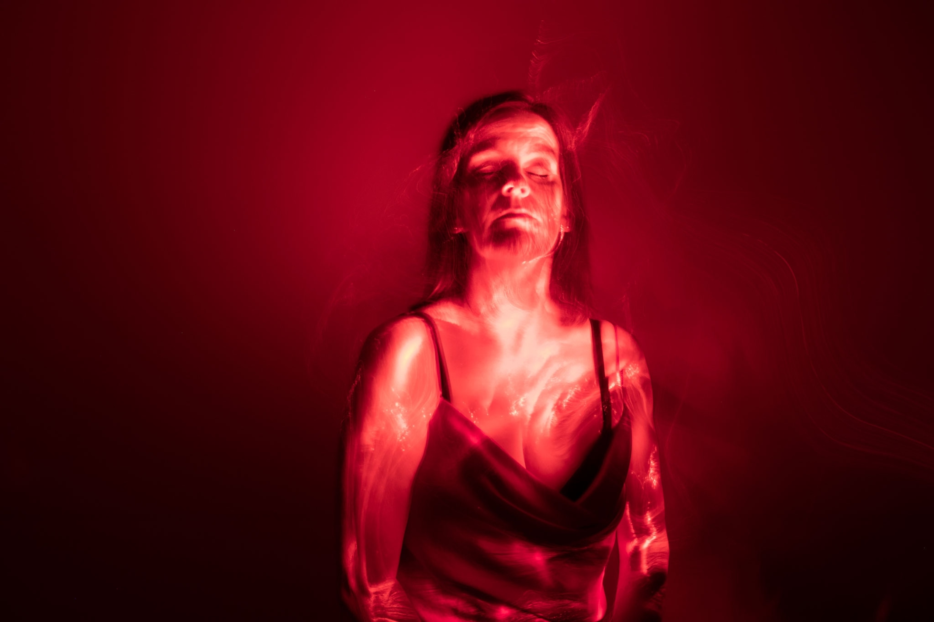 a woman pictured with closed eyes against a red backdrop and with a red glow to illustrate the symptoms of menopause