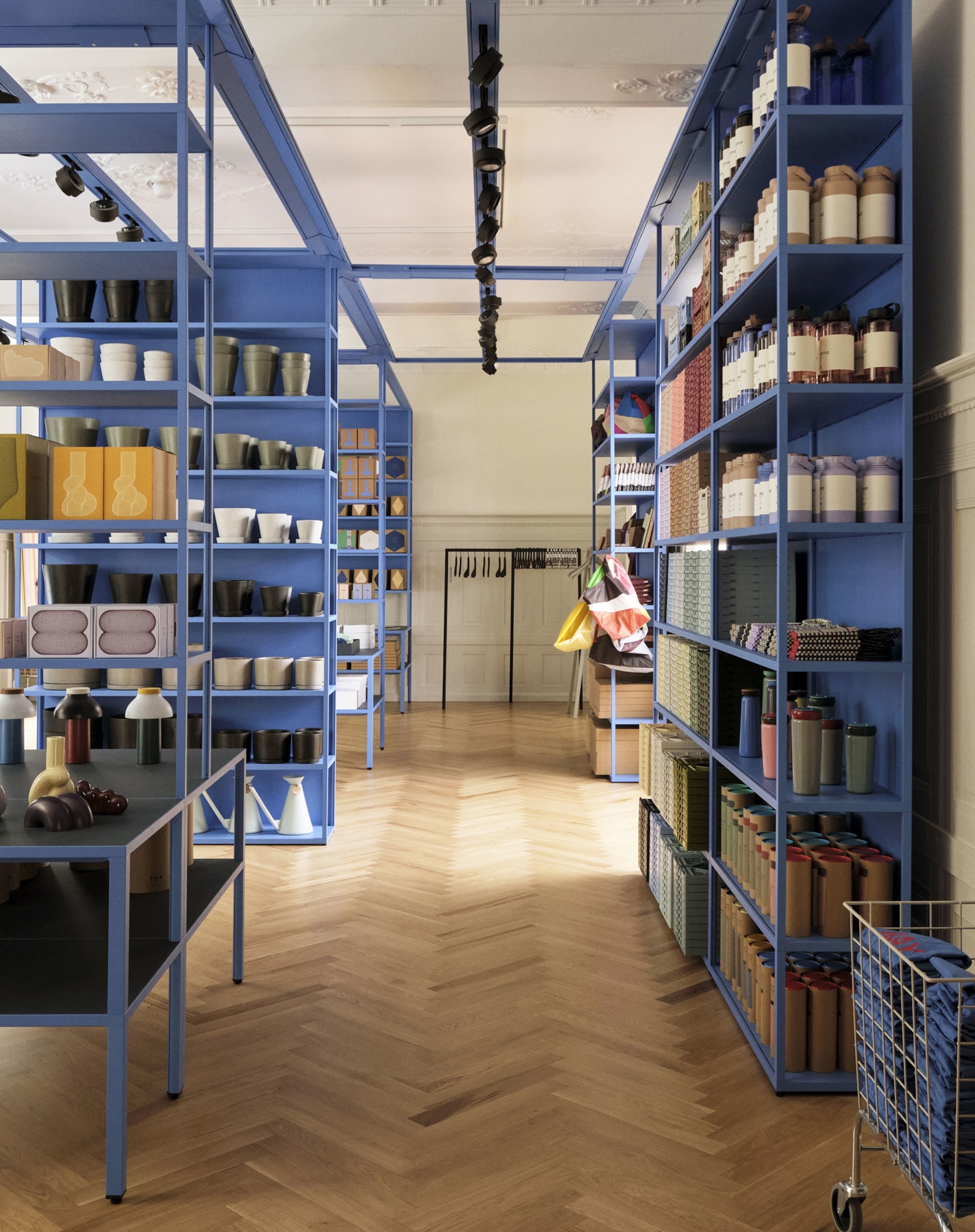 Various home accessories and design products adorn rows of bright blue shelves inside of a naturally lit room with wood floors.