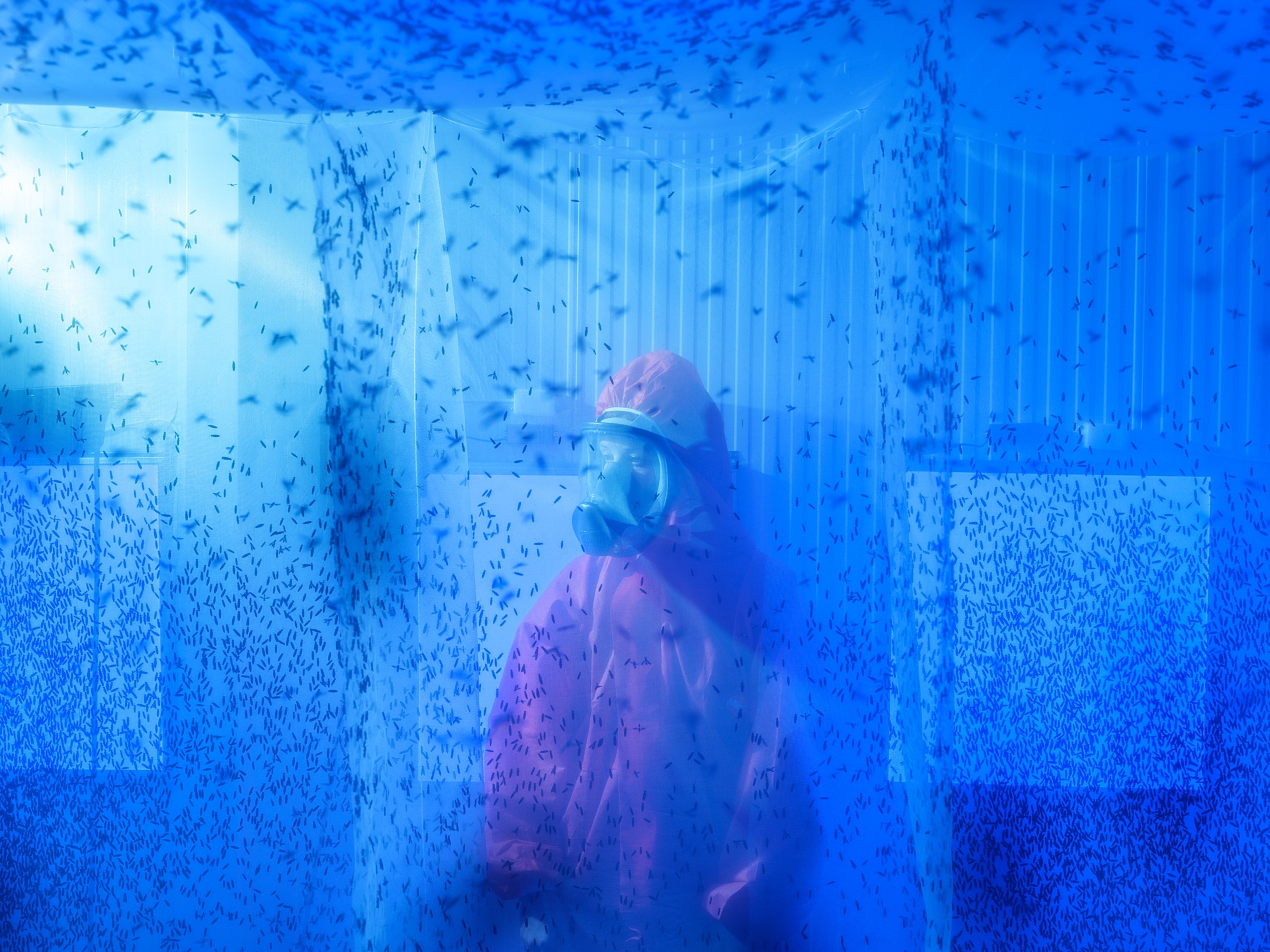A woman in a red protective suit is surrounded by a swarm of bugs in an enclosed industrial space