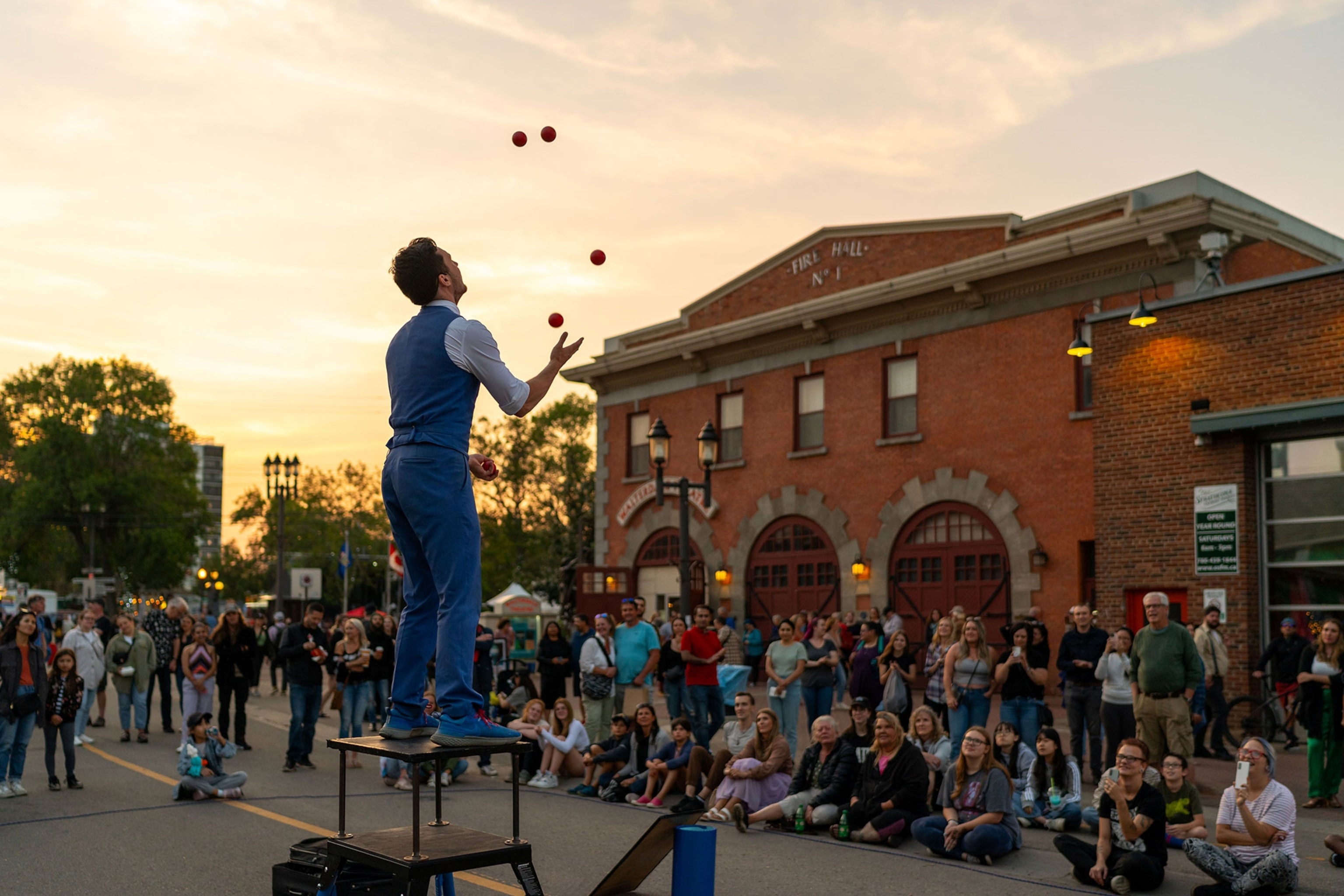 A mall stands on a platform juggling as a crowd watches.