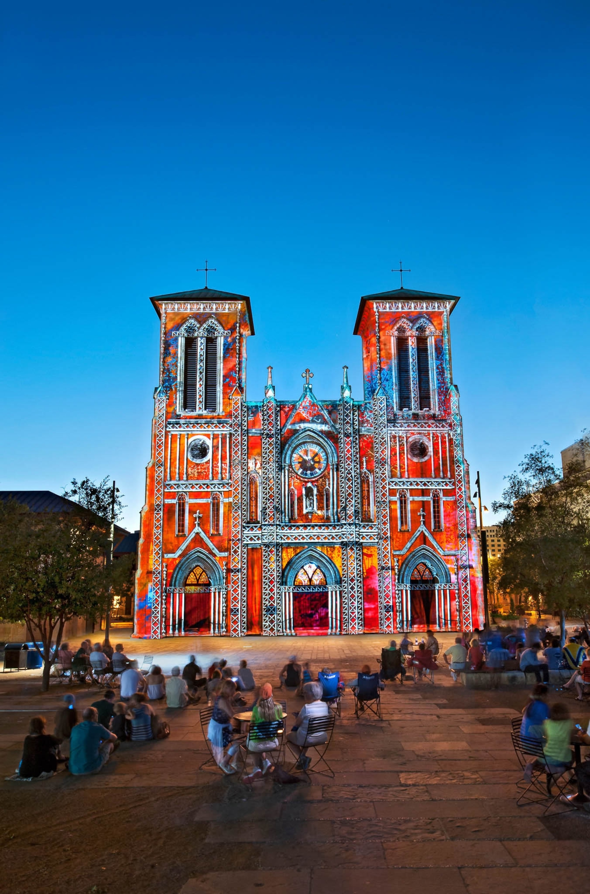 Colorful lights are displayed on church with people watching.