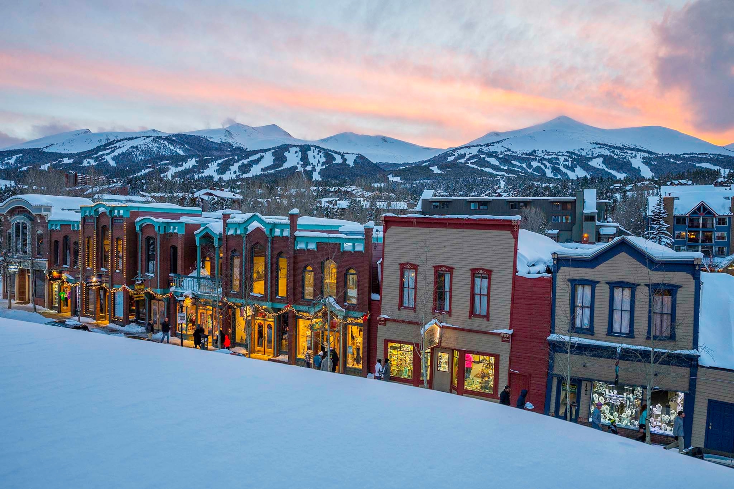 Storefronts of buildings in the snow at sunset illuminated by golden lights
