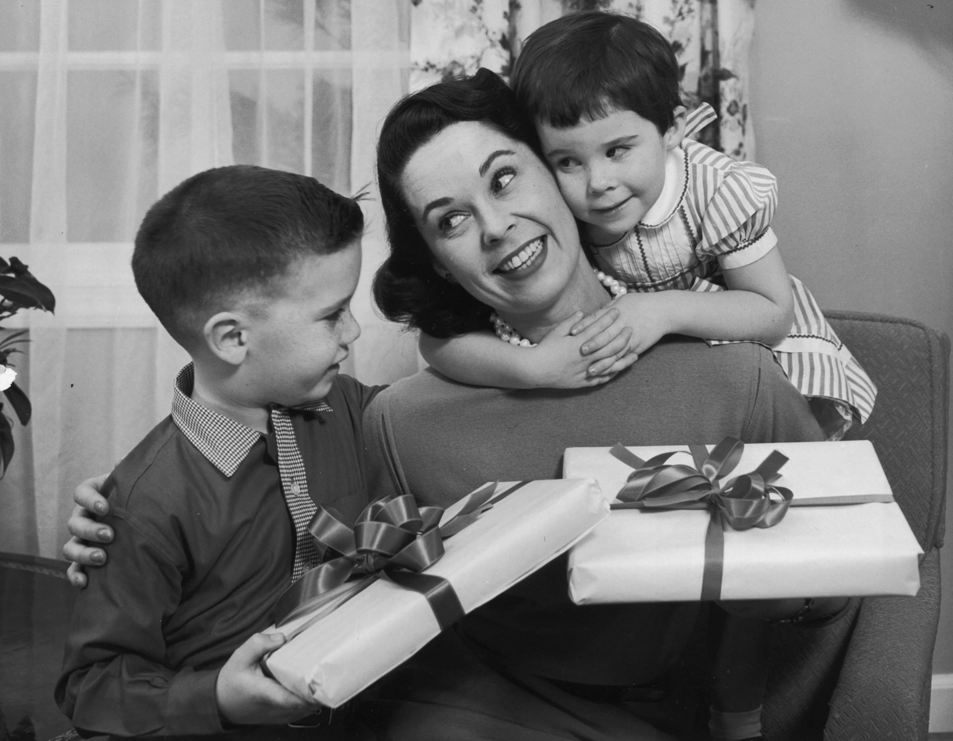 a black and white photo of two children giving their mother a present in 1955