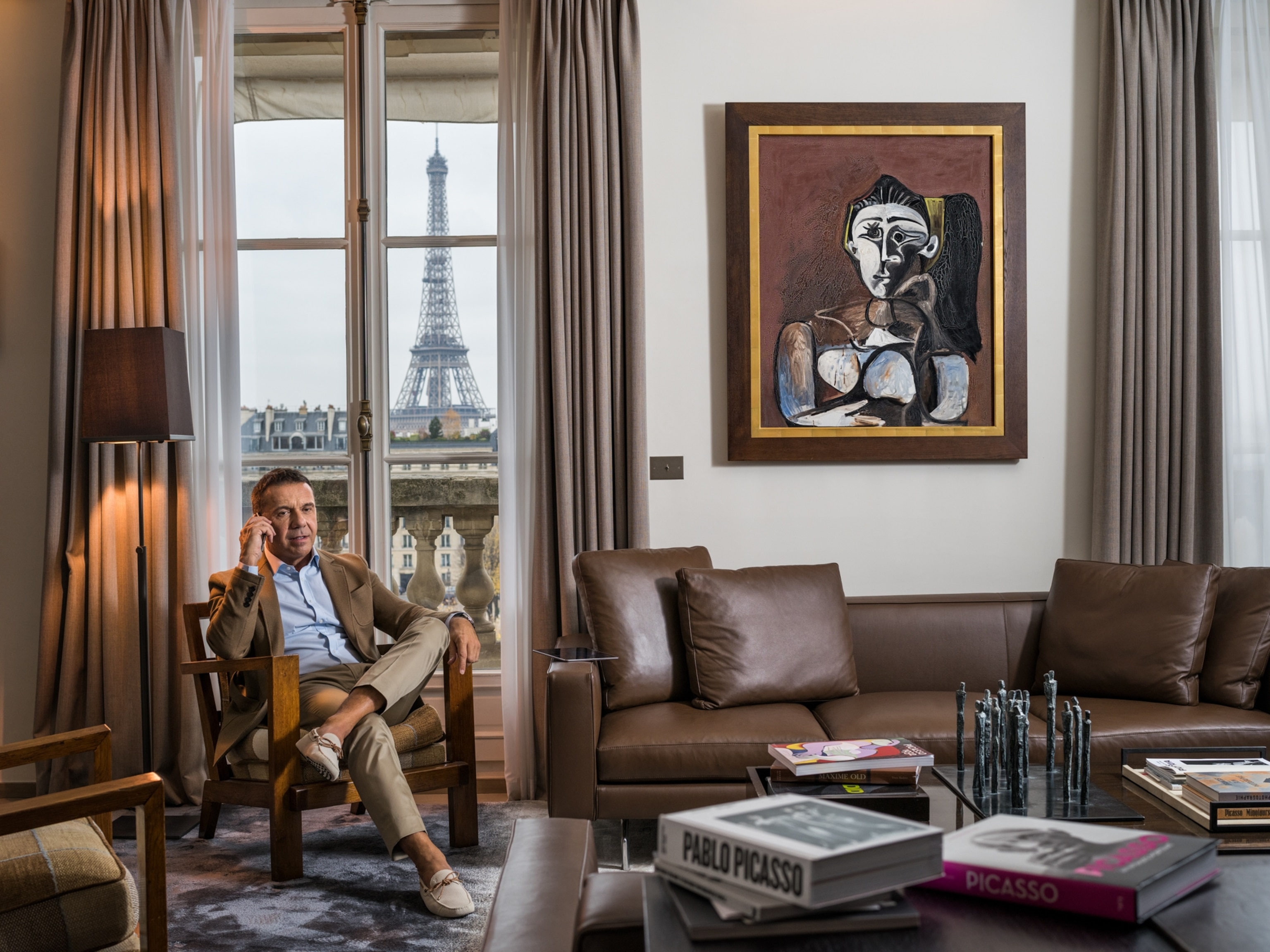 Olivier Picasso sitting near a Picasso painting with the Eiffel tower outside the window