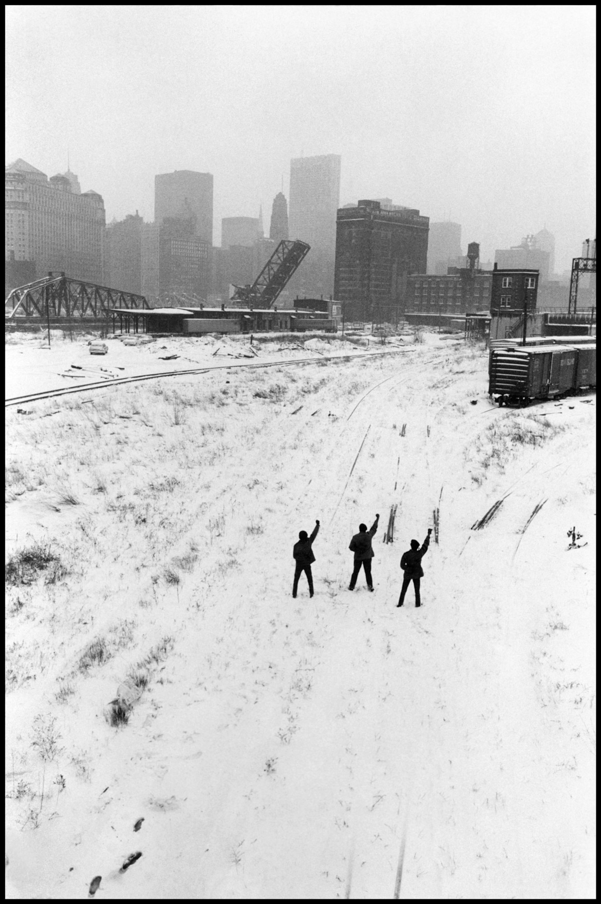 three men raising their fist in the snow with the Chicago skyline in the background