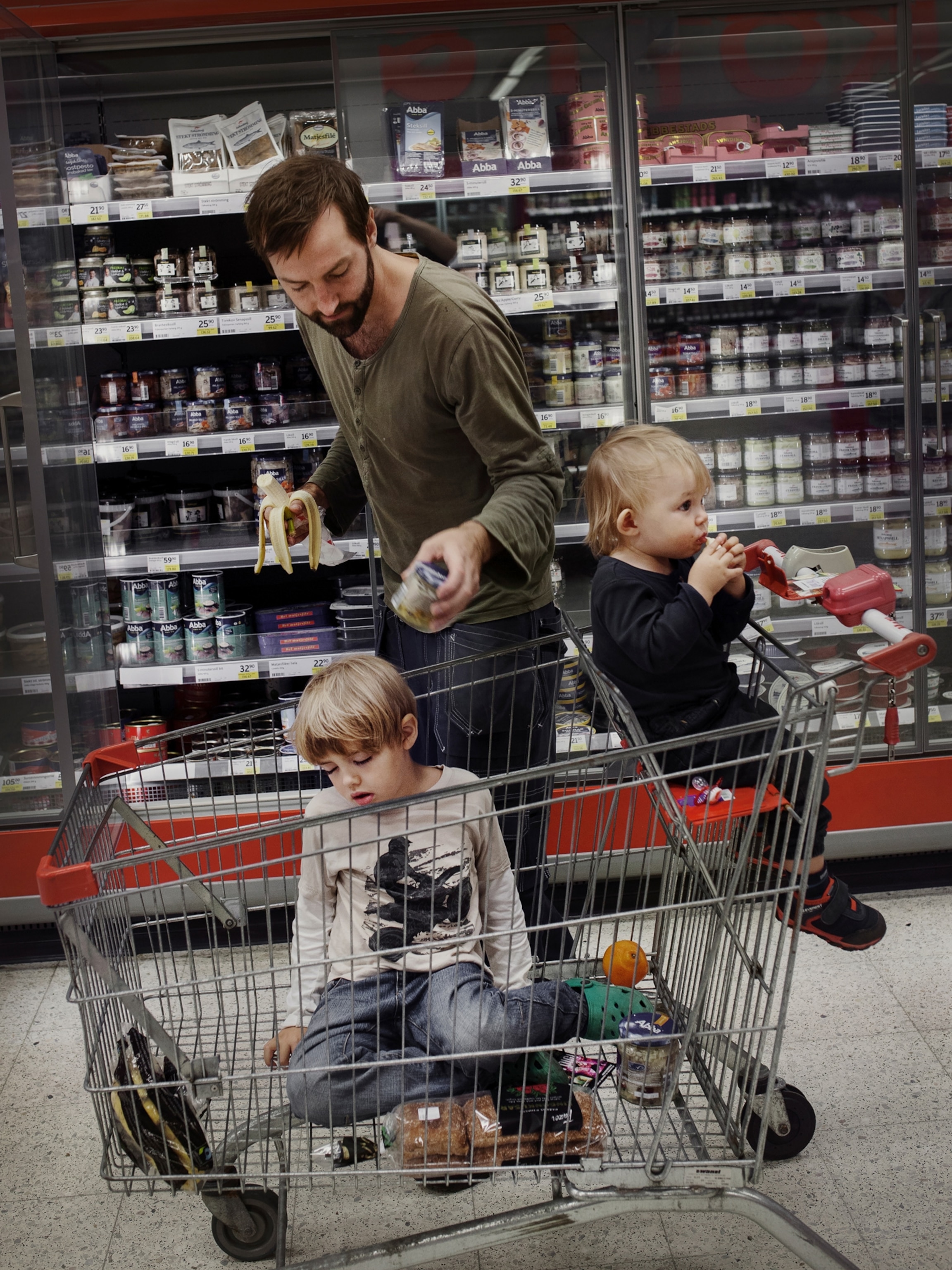 a father grocery shopping with his two children in the shopping cart