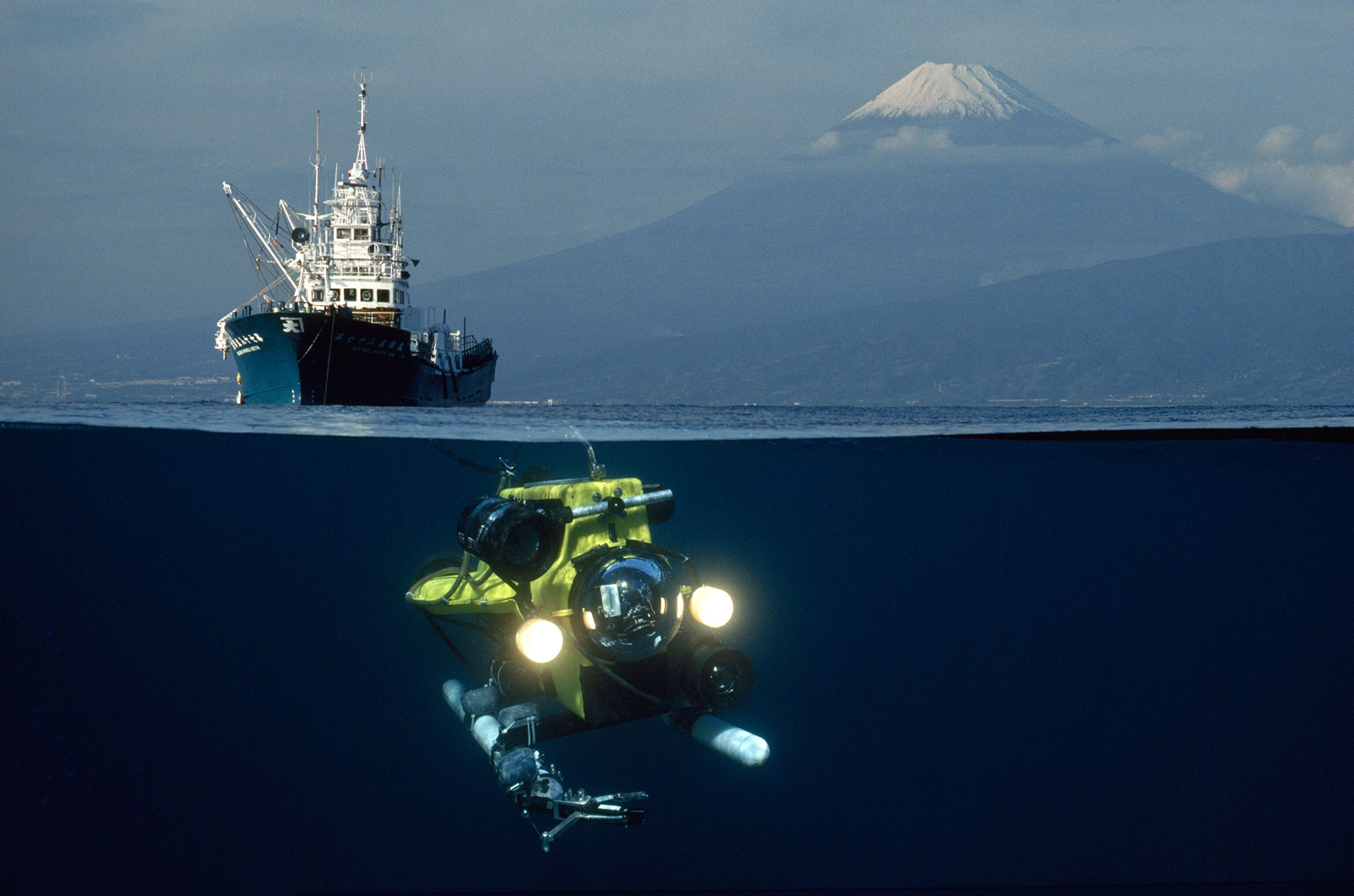 Picture that's half underwater of an ROV and a ship with Mt Fuji in the background