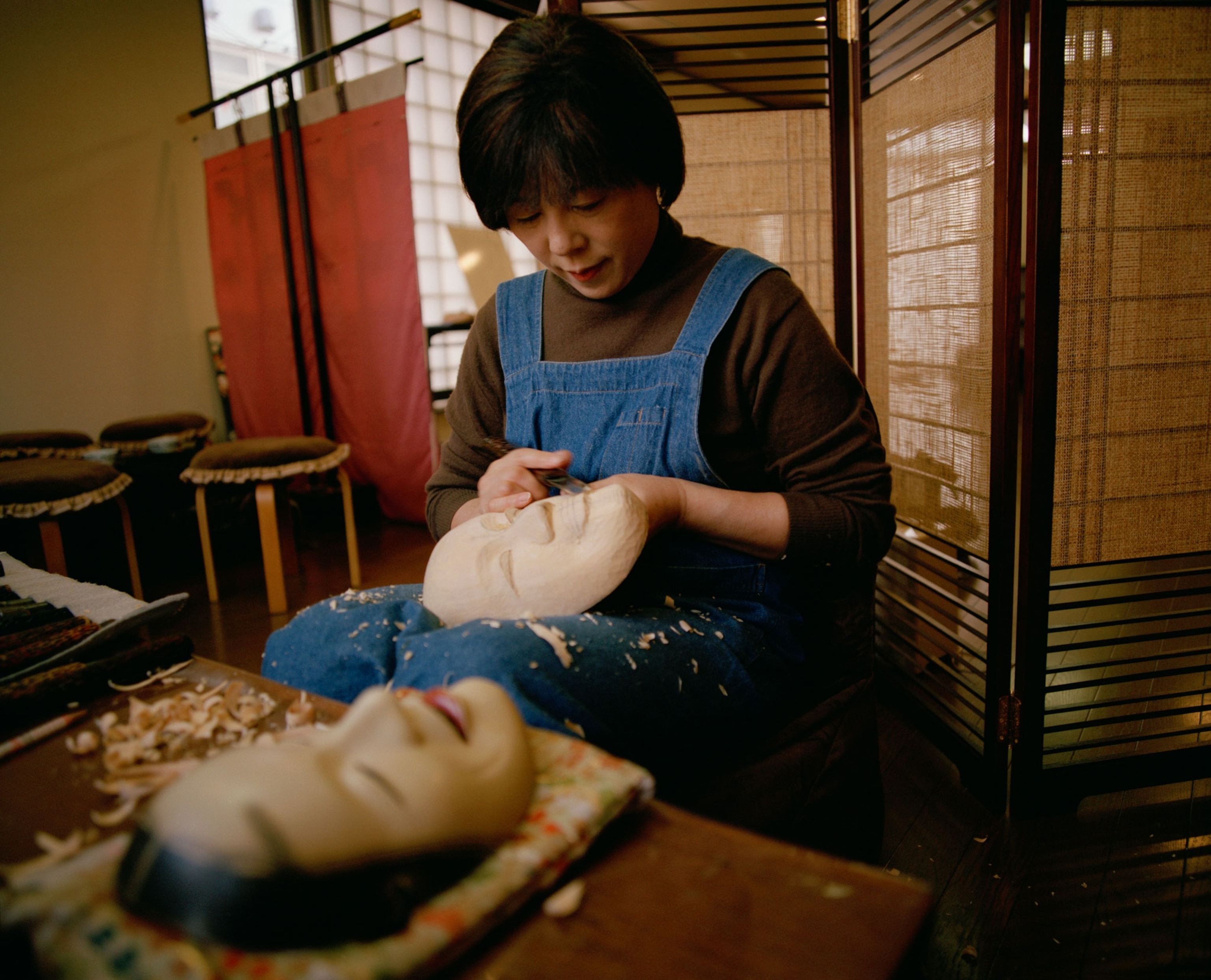 a woman working on a wooden noh theatre mask