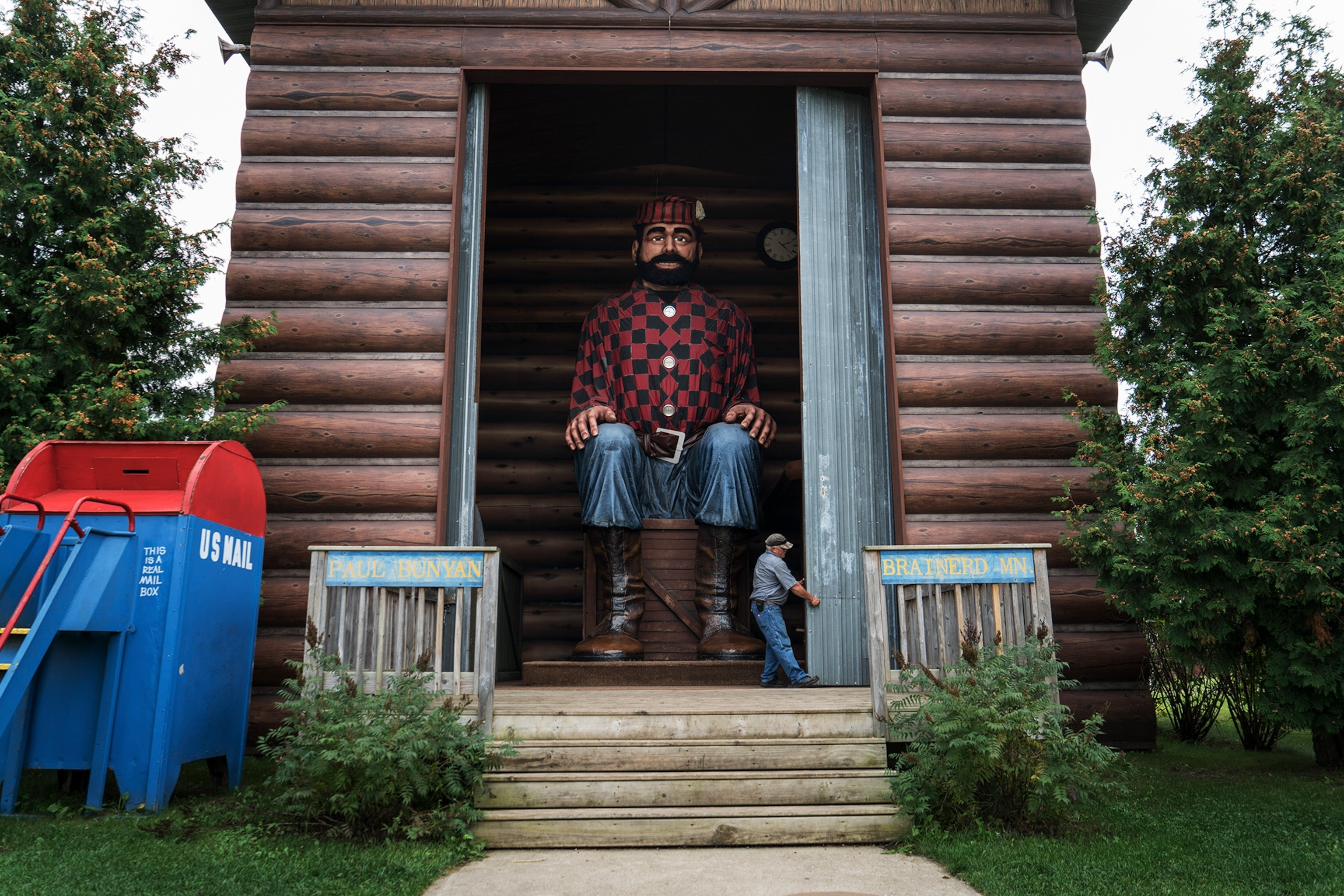 A man closes a shed door containing a larger-than-life Paul Bunyan.