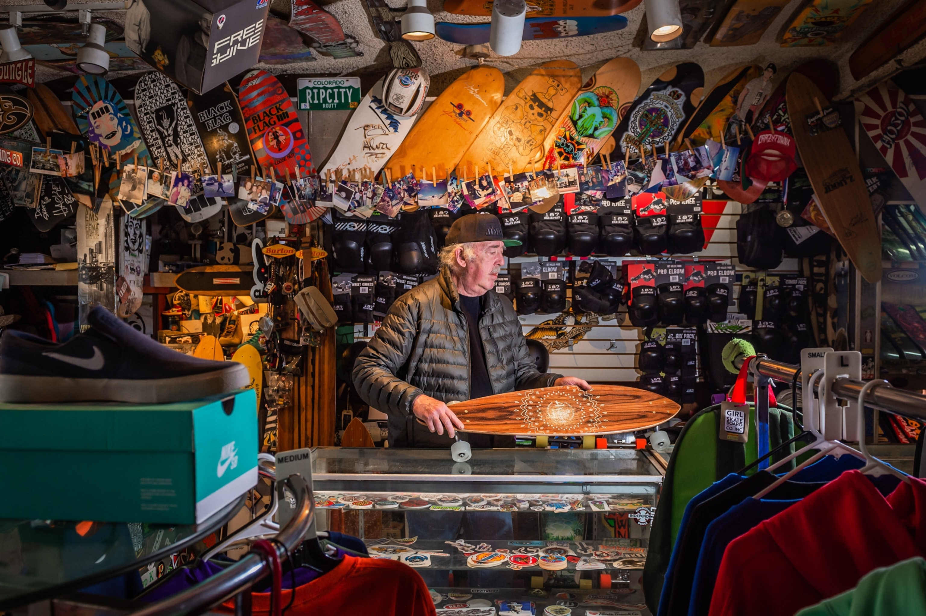 a shop owner holding a skateboard in his board-covered shop