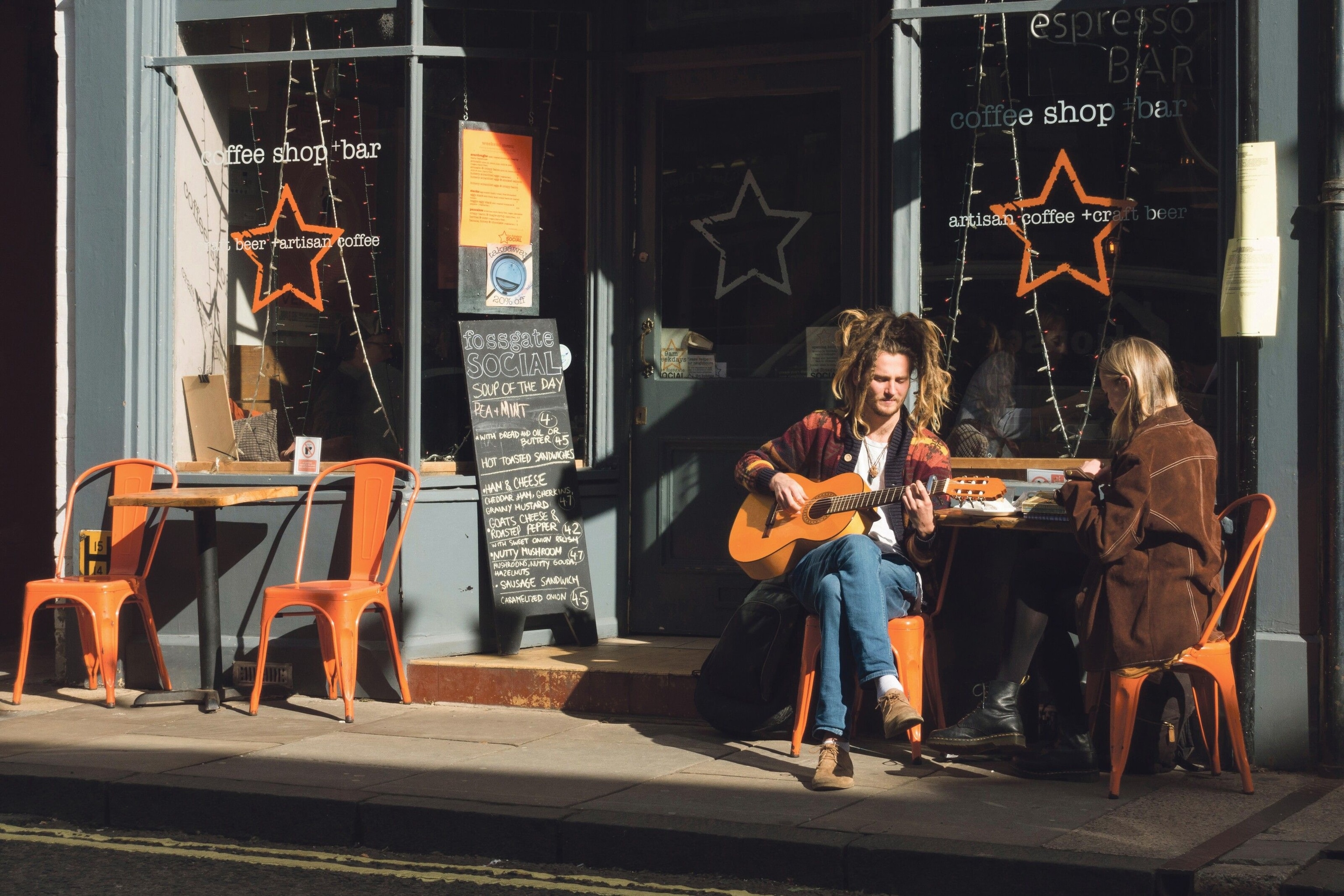 A young couple sit in sun outside Fossgate Social coffeehouse and bar.