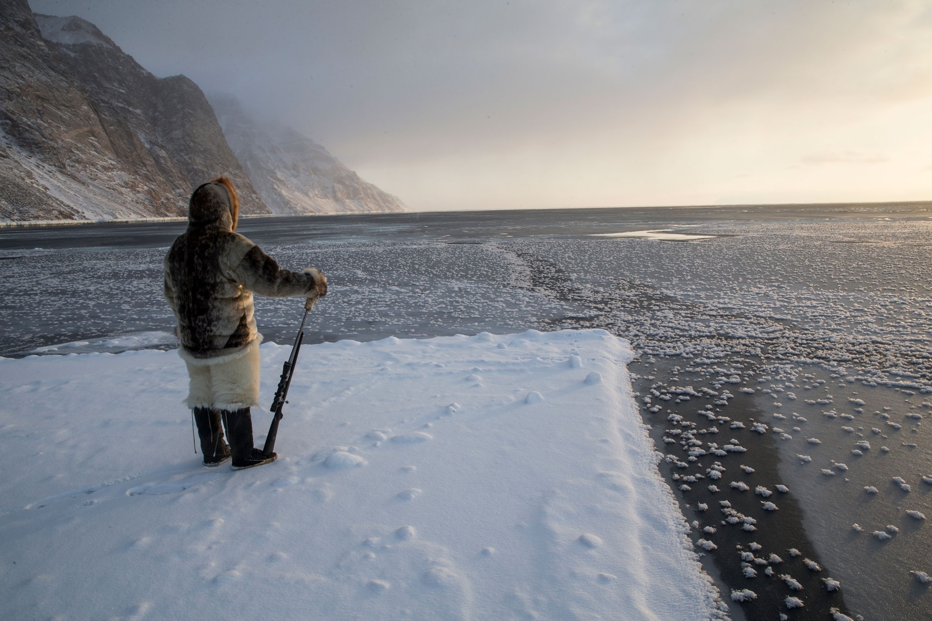 An Inuit hunter stands on the surface of an iceberg to assess the seascape.