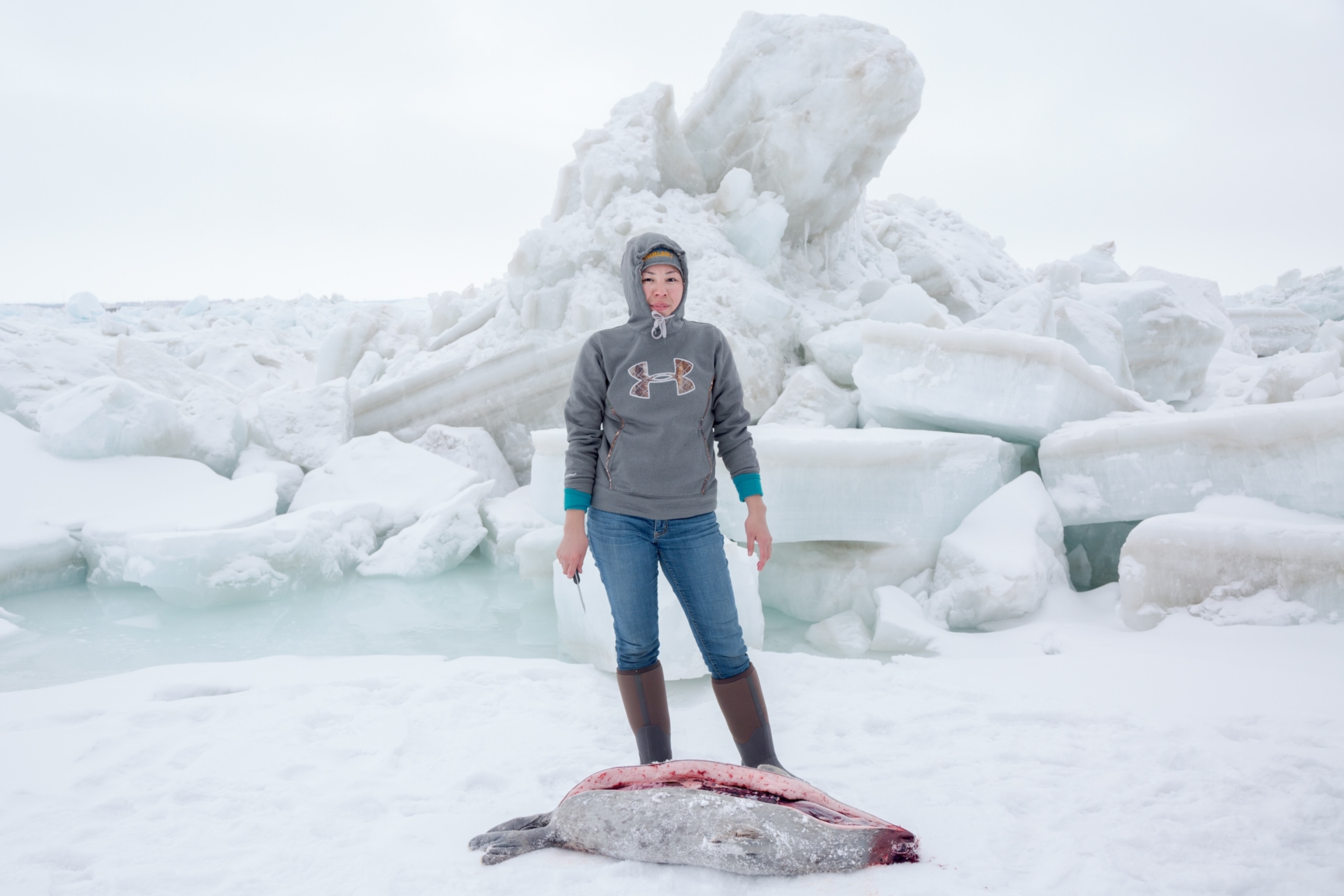 young Inupiat woman with knife standing over a seal she is butchering.