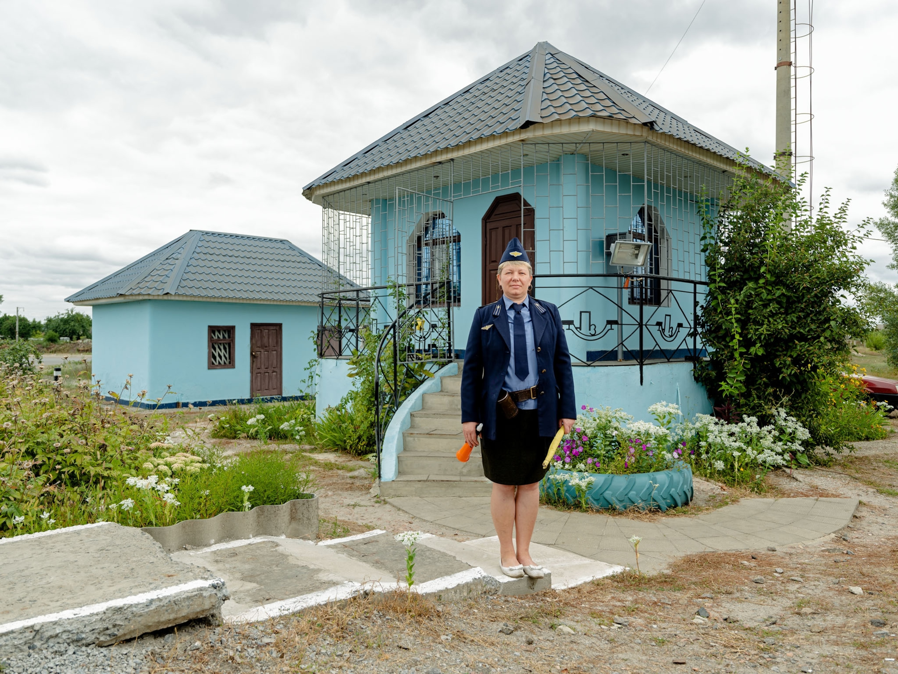 woman in uniform by small blue house with fancy iron porch railing.